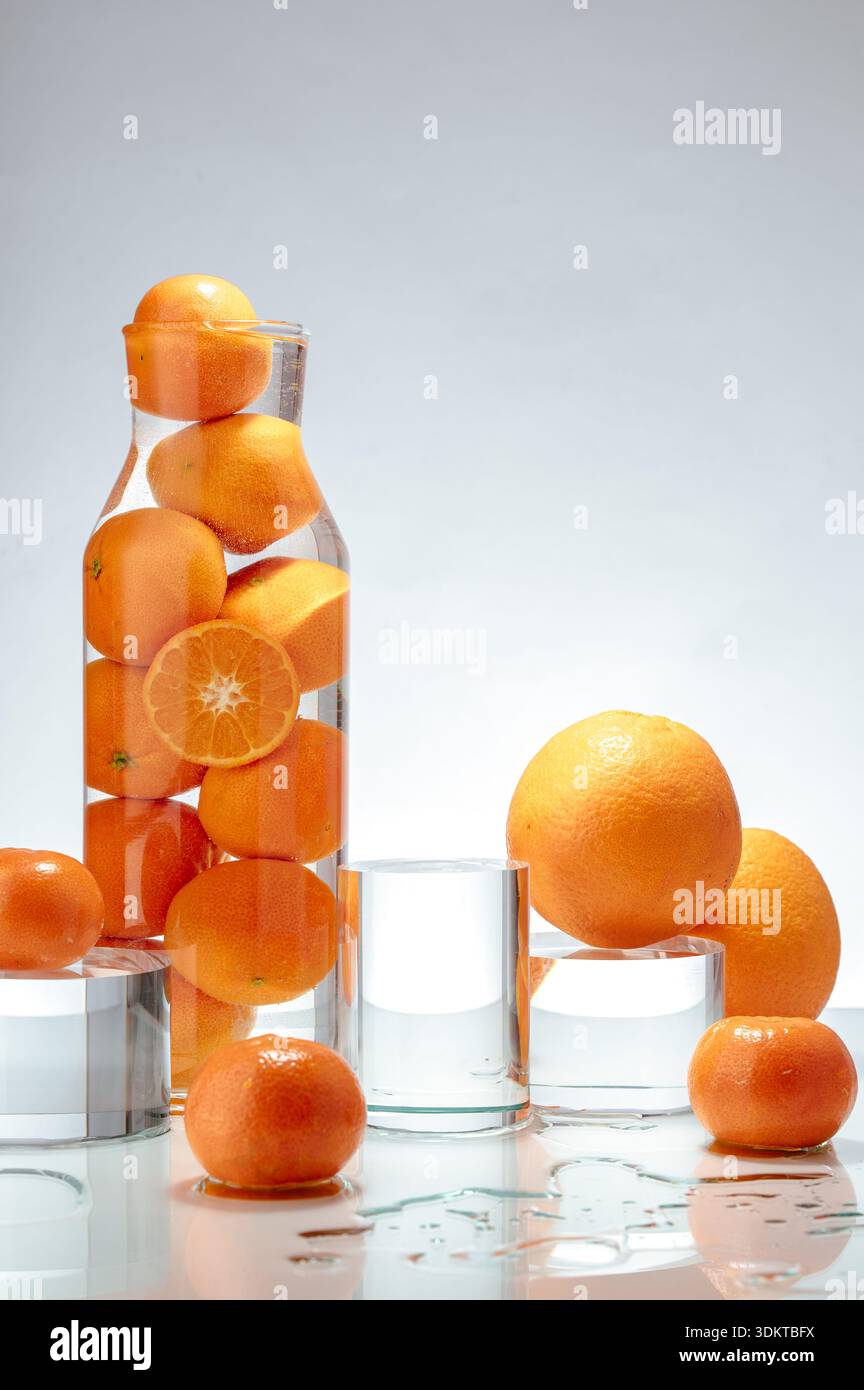Orangen und Mandarinen in einem Glasgefäß und auf einem Tisch. Stockfoto
