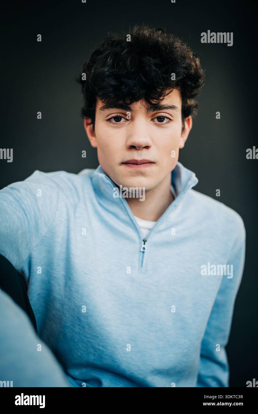 Ernster junger Mann in hellblauem Pullover vor dunklem Hintergrund Stockfoto