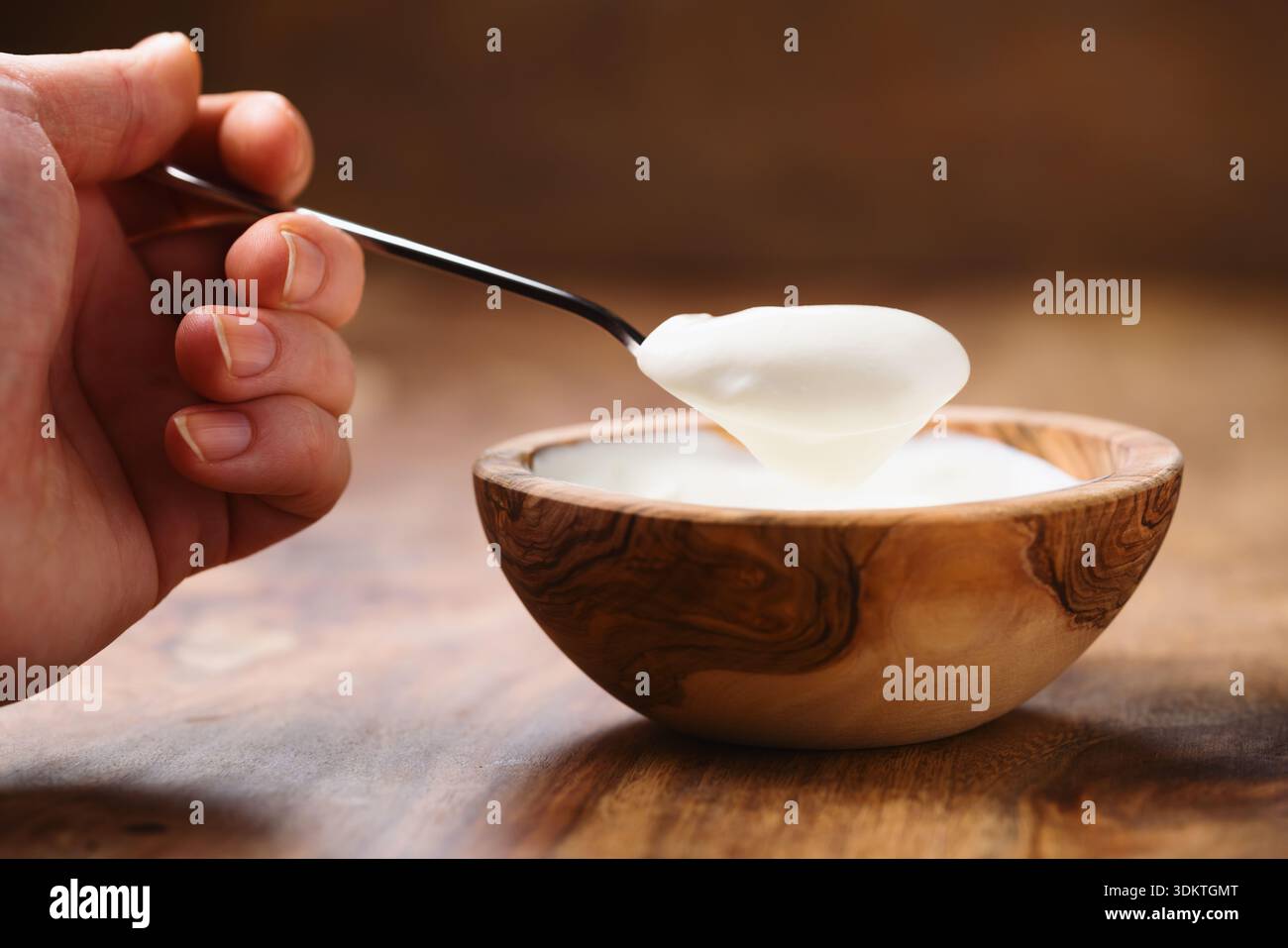 POV-Schuss junger weiblicher Hand mit vollem Löffel Joghurt am Tisch Stockfoto