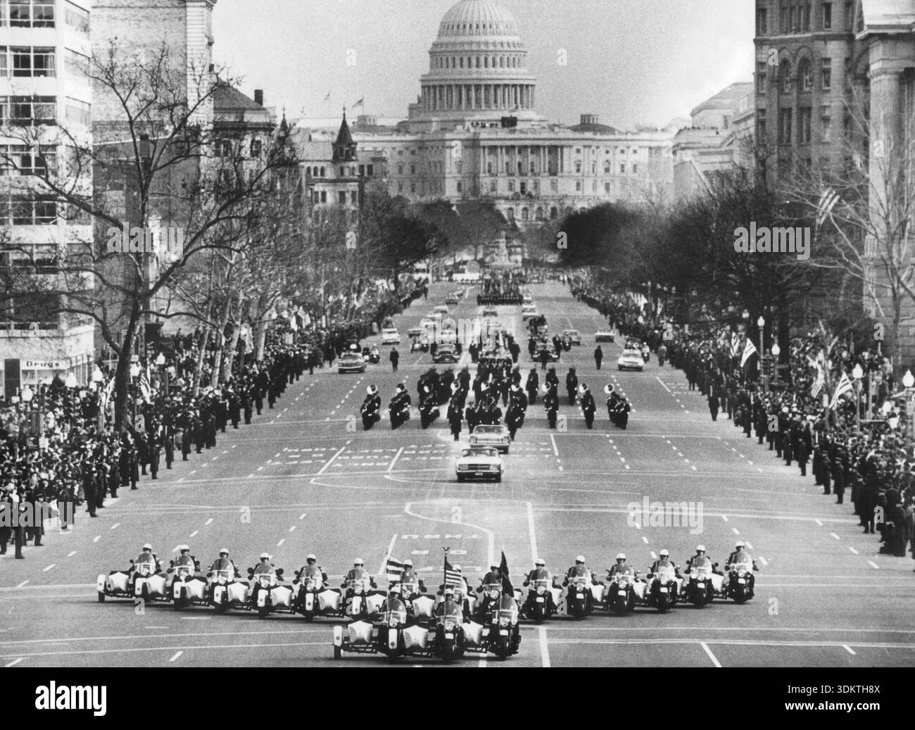 Parade auf der Pennsylvania Avenue bei der Amtseinführung von Lyndon Baines Johnson nach seiner Wiederwahl zum Präsidenten. Die Parade führt vom Kapitol (im Hintergrund) zum Weißen Haus. Die Limousine, in der der Präsident fährt, wird von einer Gruppe von Motorradpolizisten begleitet. Auf die Präsidentenlimousine folgt eine Blaskapelle. [Automatisierte Übersetzung] Stockfoto