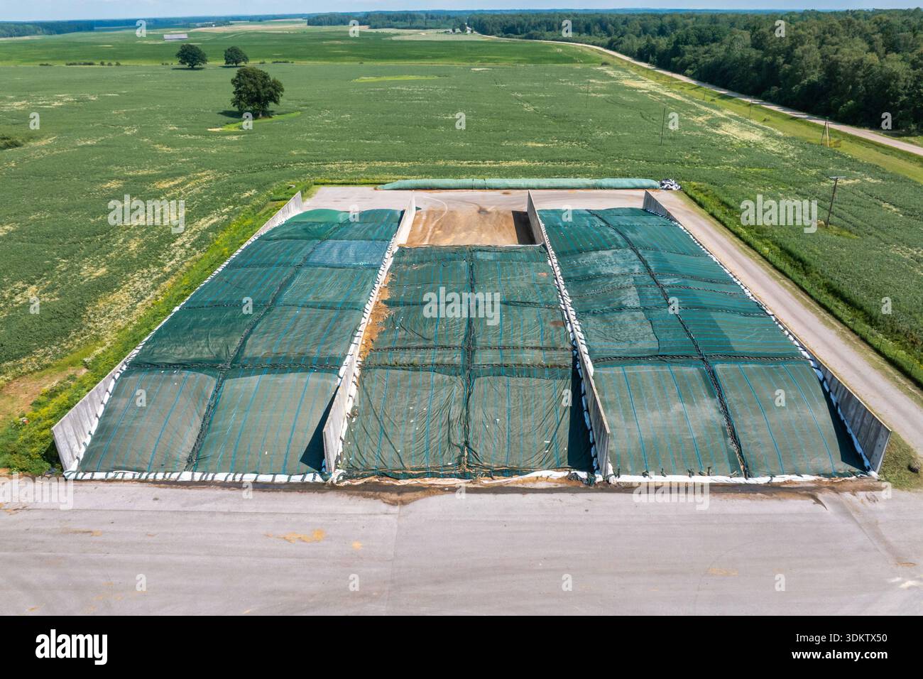 Die Luftaufnahme zeigt drei Betonsilage-Bunker mit grünen Gitterabdeckungen, eine teilweise freigelegte Bucht, neben geraden Schotterstraßen und Getreidefeldern in der Mitte Stockfoto