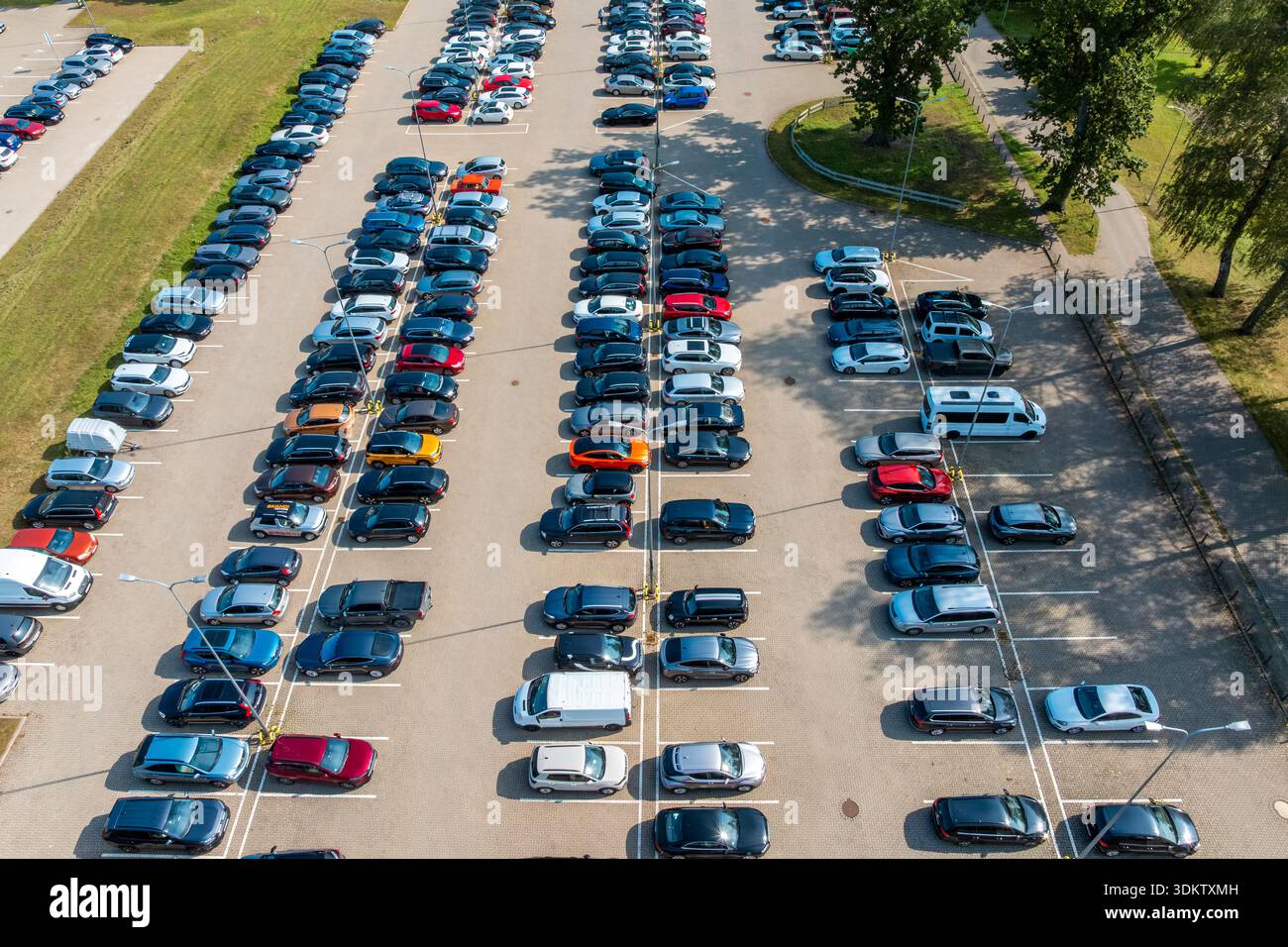 Eine erhöhte Perspektive auf einen Parkplatz mit sauber angeordneten Autos, verschiedenen Farben und Modellen, Straßenlaternen und Bäumen an den Kanten. Stockfoto