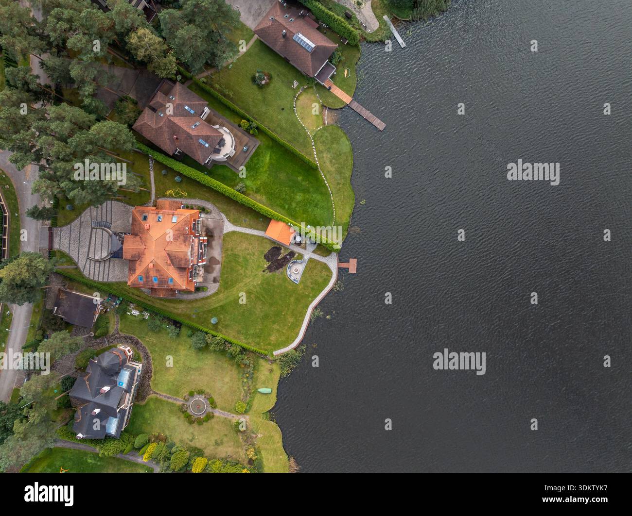 Eine Gruppe von Häusern mit einzigartigem Design, darunter ein orangefarbenes Dachgebäude, Rasenflächen, Wege und private Docks, die sich in ein großes Gewässer erstrecken. Stockfoto