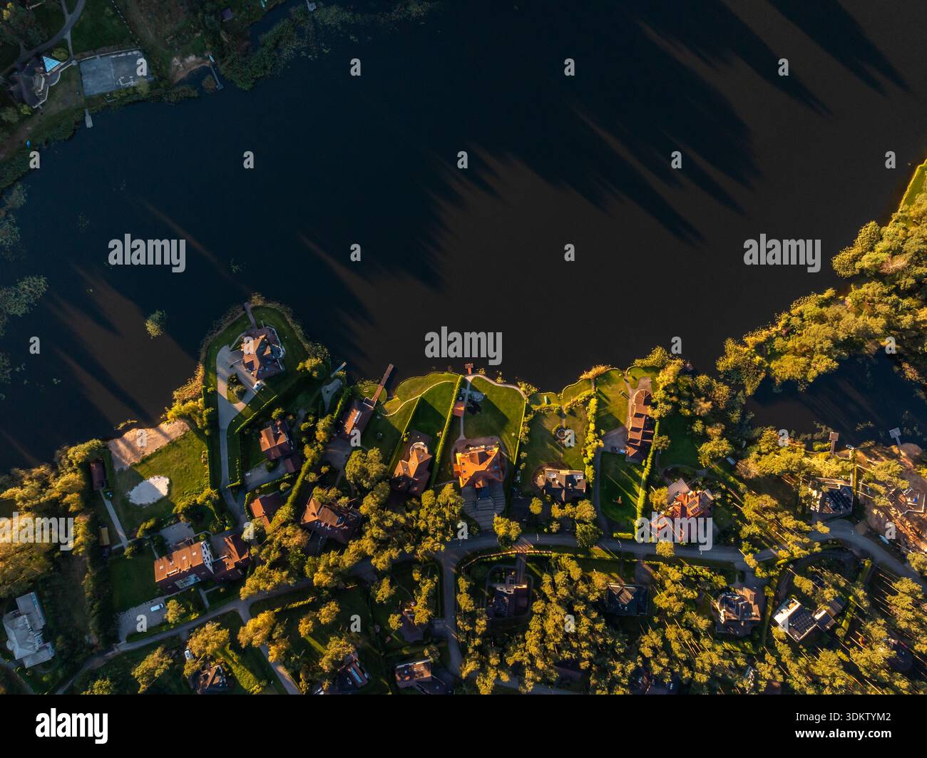 Aus der Vogelperspektive eines Viertels mit gewundenen Straßen, gepflegten Rasenflächen und Bäumen in der Nähe eines unregelmäßig geformten dunklen Wasserkörpers. Stockfoto