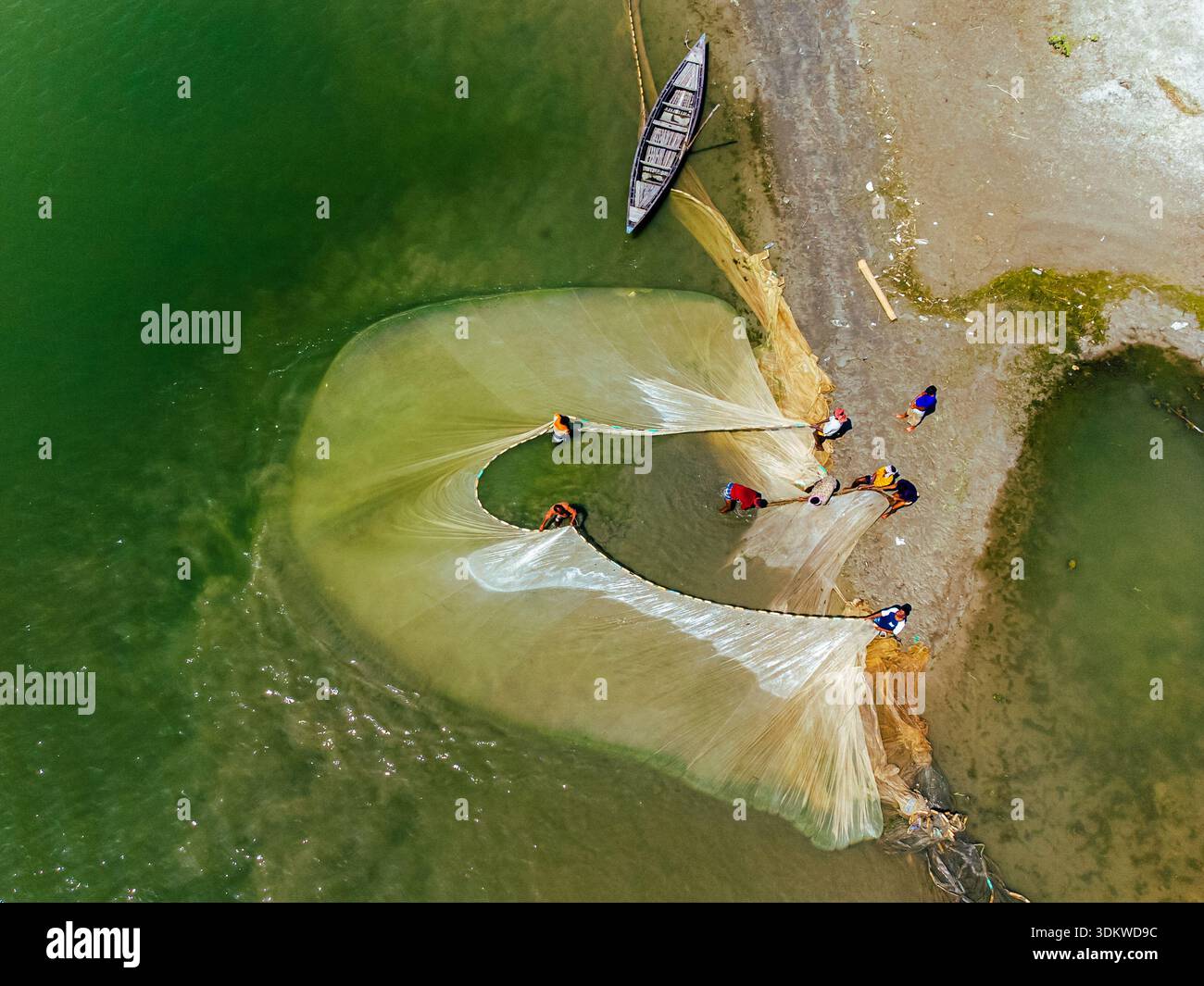 Aus der Vogelperspektive sehen Fischer, die ihre Netze in den flachen Gewässern werfen, ein Boot ruht auf dem Sandufer, Bogura, Bangladesch. Stockfoto
