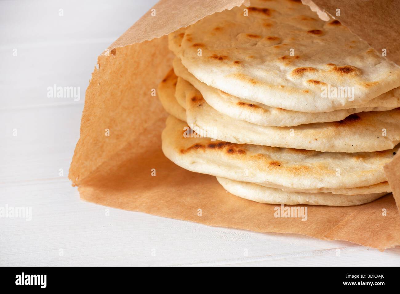 Hausgemachtes Fladenbrot in einer braunen Papiertüte auf weißem Holzhintergrund. Umweltfreundliche, biologisch abbaubare Recycling-Lebensmittelverpackungen. Stockfoto