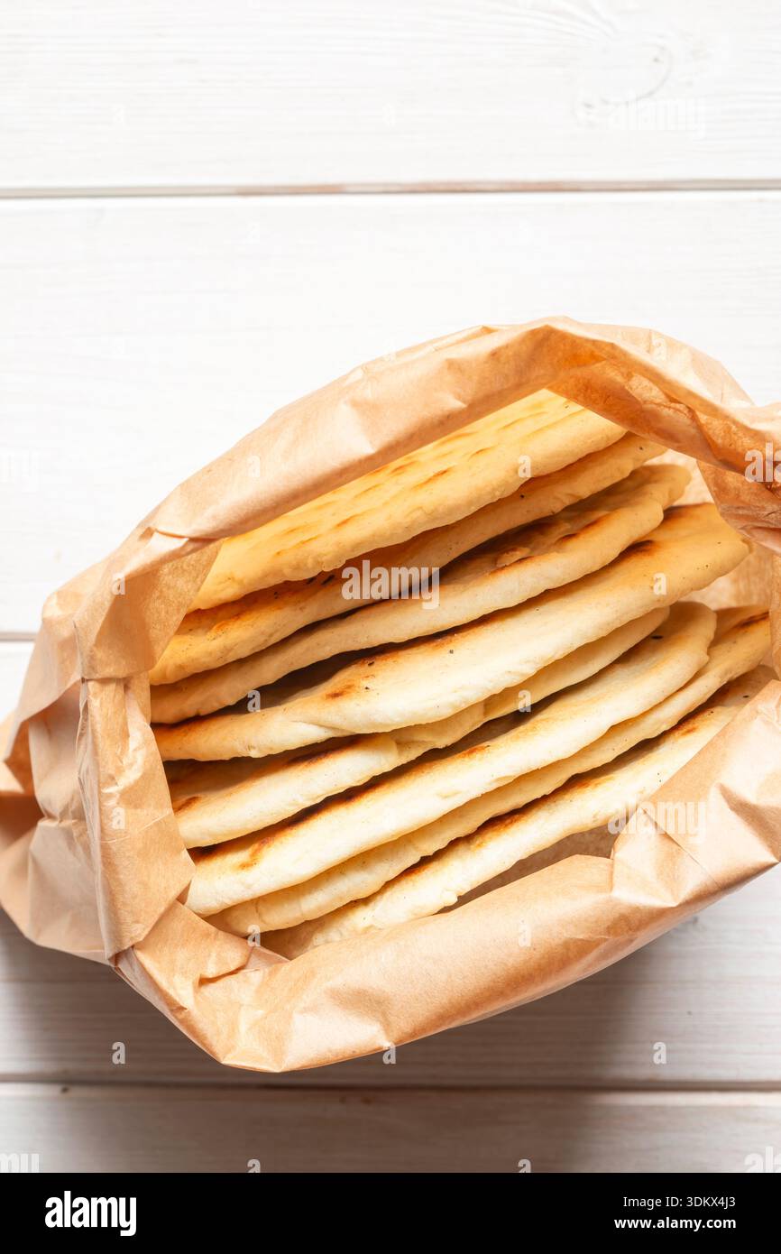 Hausgemachtes Fladenbrot in einer braunen Papiertüte auf weißem Holzhintergrund. Umweltfreundliche, biologisch abbaubare Recycling-Lebensmittelverpackungen. Stockfoto