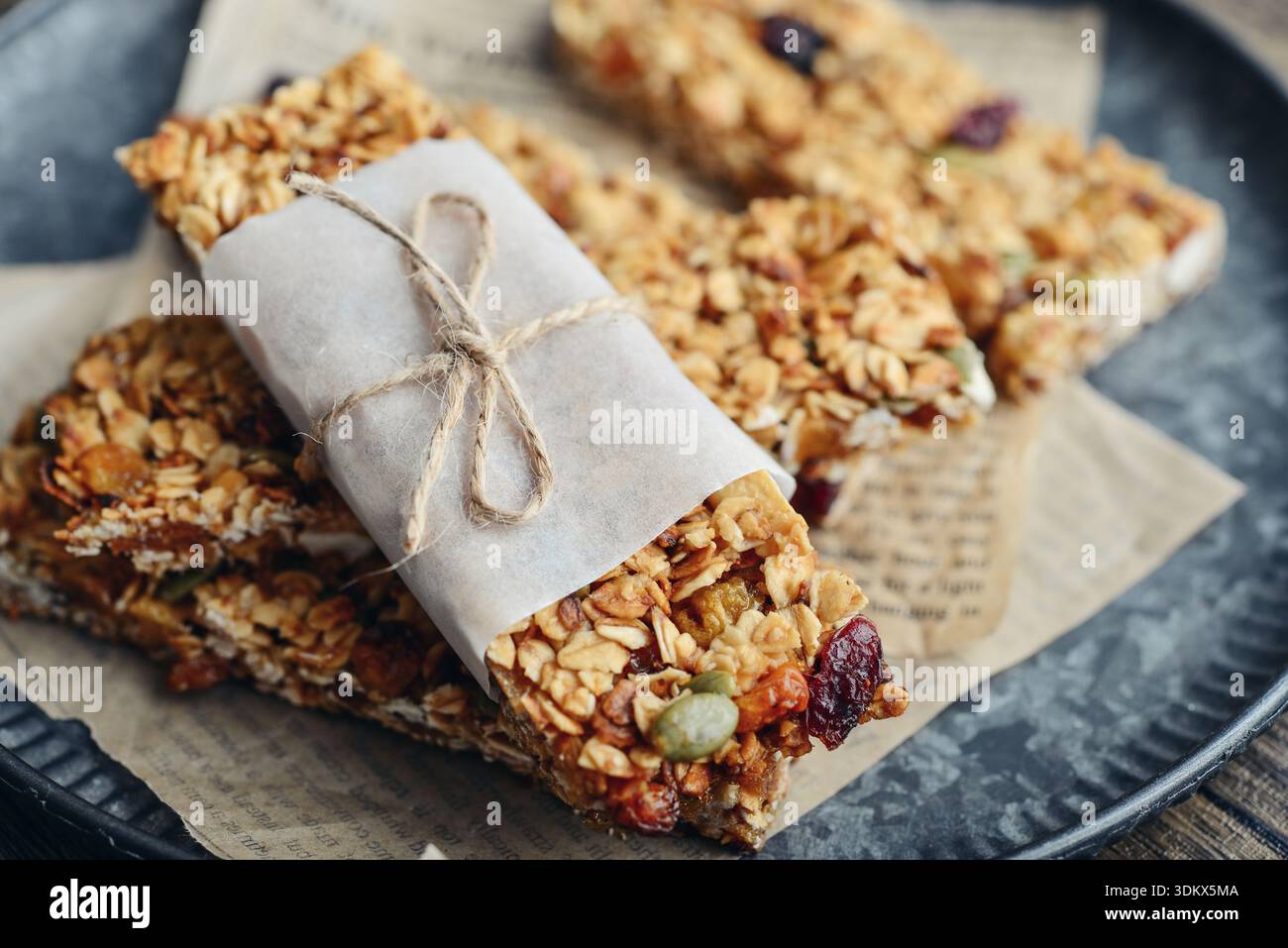 Glutenfreier Hafer-Müsliriegel mit Nüssen und Beeren auf rundem Vintage-Metalltablett auf hölzernem Hintergrund, Nahaufnahme Stockfoto
