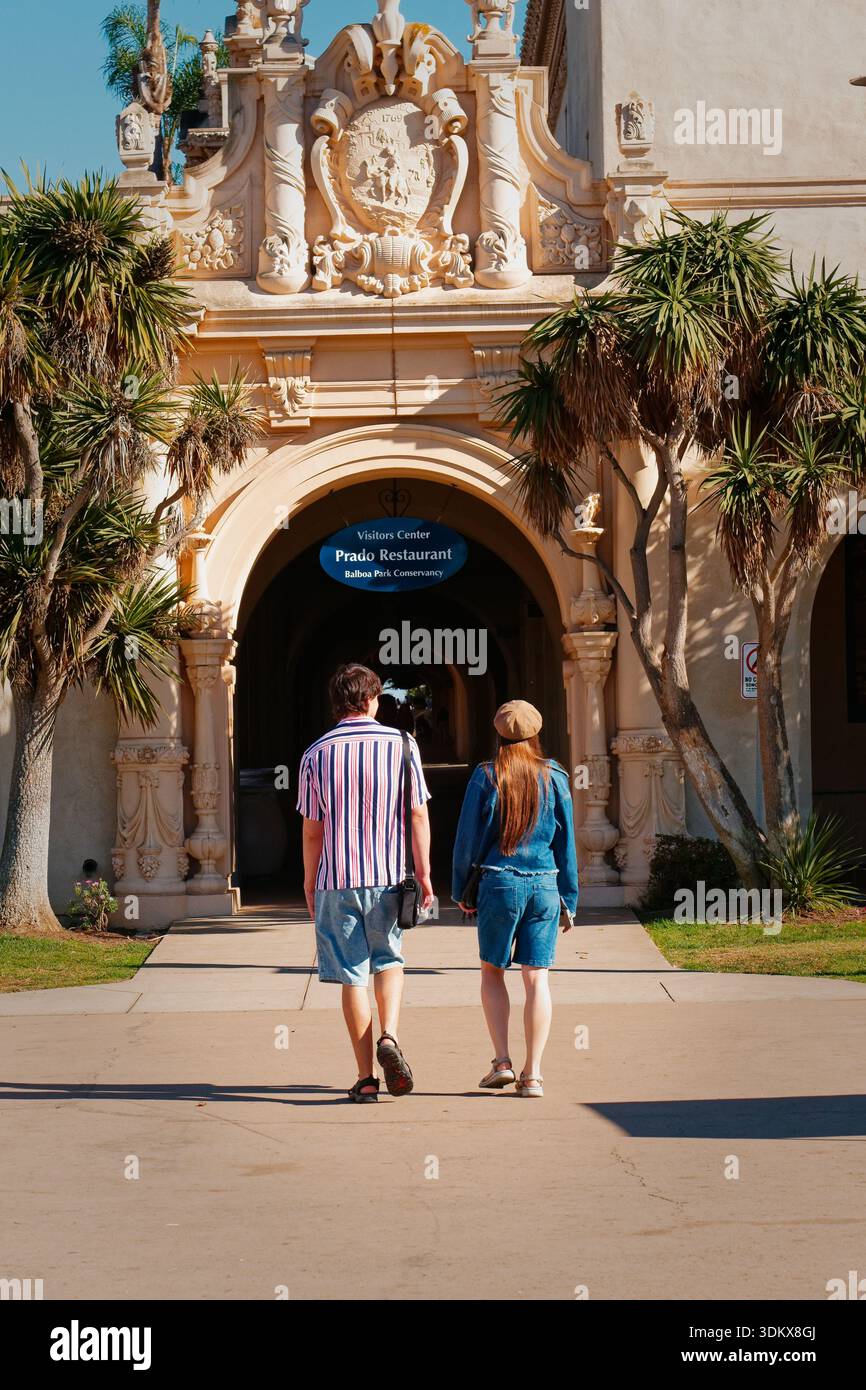 Duo Bewegt Sich Gemächlich In Richtung Eingang, Inmitten Von Texturierten Steinfassaden Unter Hellem Spanischem Sonnenlicht Stockfoto