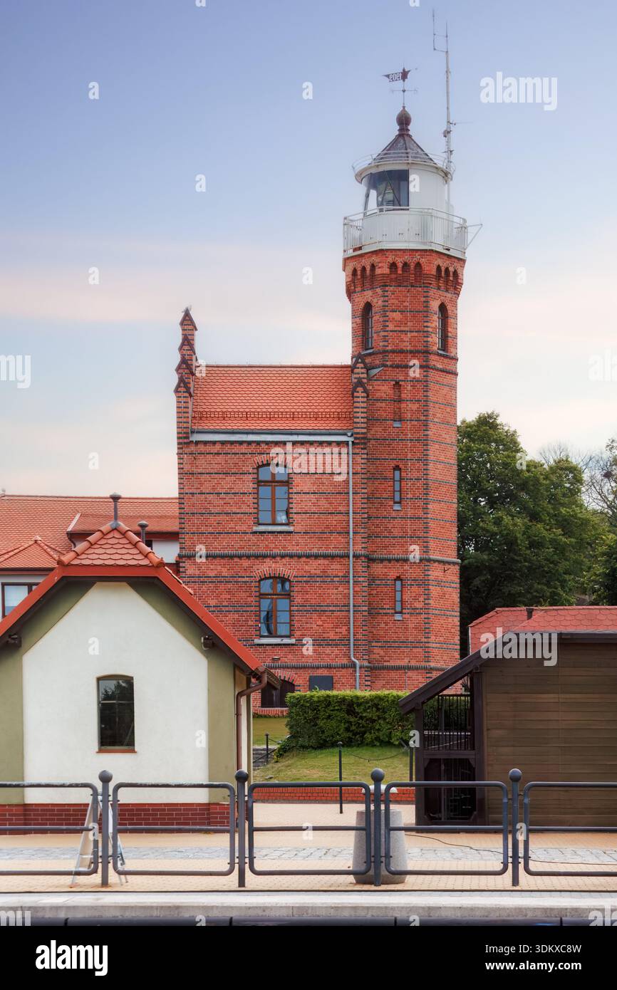 Historischer Leuchtturm aus rotem Backstein, der sich über kleinen Küstengebäuden erhebt, Symbol der Schifffahrt und Kontinuität, die die maritime Identität von Ustka, Polen Ao, prägt Stockfoto