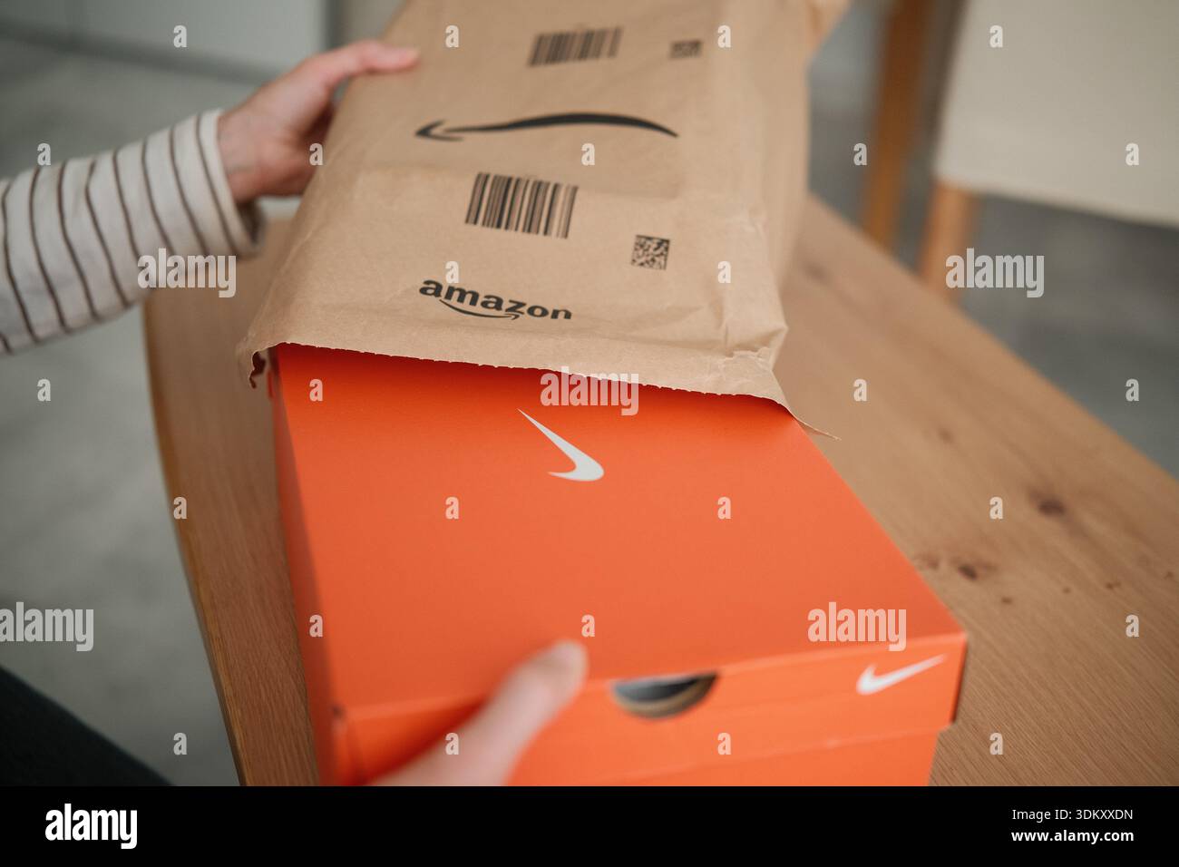 Alicante, Spanien - 02. Februar 2026: Frau packt eine Amazon-Lieferung zu Hause aus. Das Paket enthält einen leuchtend orangefarbenen Nike Schuhkarton Stockfoto