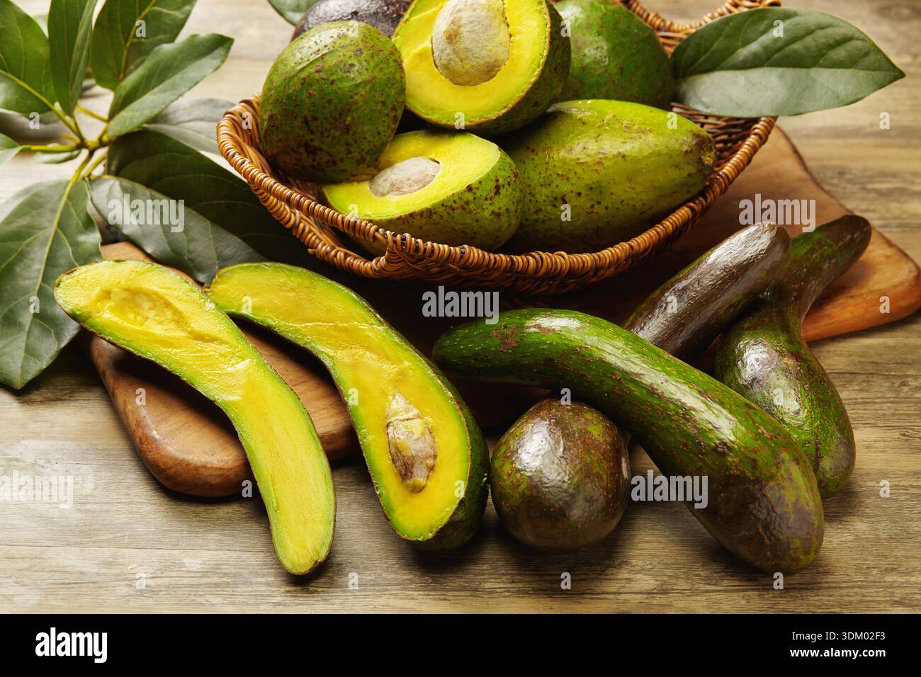 Frische, reife Avocados auf einem rustikalen Holztisch mit ganzen und geschnittenen Früchten mit lebendigem grünem Fleisch und natürlichen Texturen. Stockfoto