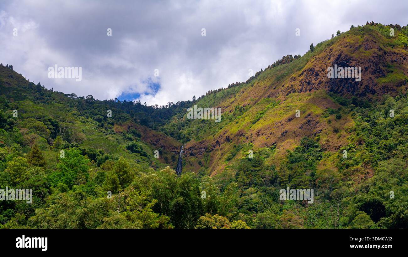 Wunderschöner Wasserfall aus der Ferne in halbtrockenen Gebirgszügen unter bewölktem Tageskaskaden von Baumköpfen ist deutlich zu sehen Stockfoto
