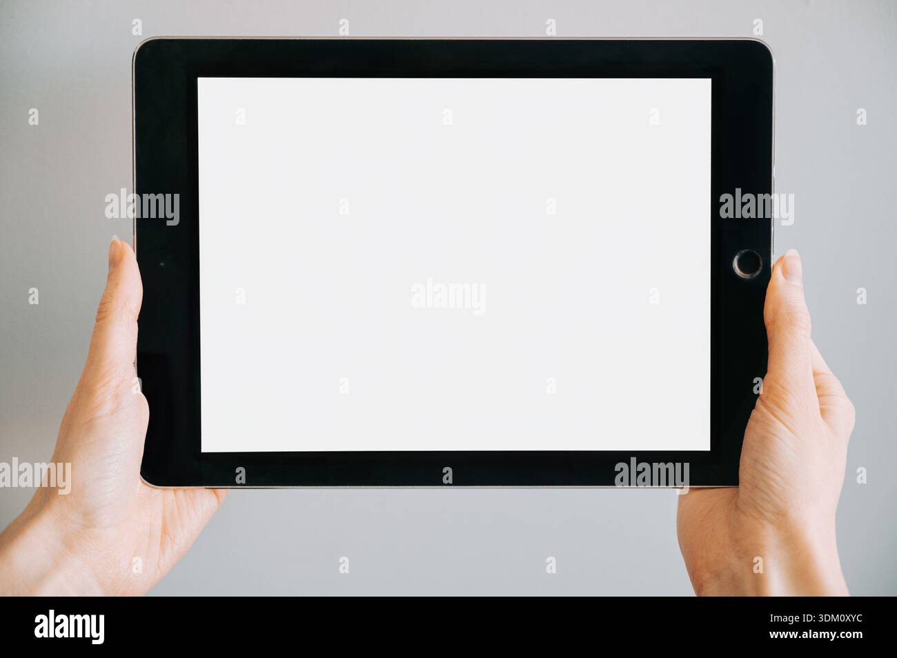 Hände, die ein modernes Tablet mit einem leeren weißen Bildschirm auf neutralem Hintergrund halten. Minimalistisches Mockup-Bild, geeignet für die Präsentation von Apps und Websit Stockfoto