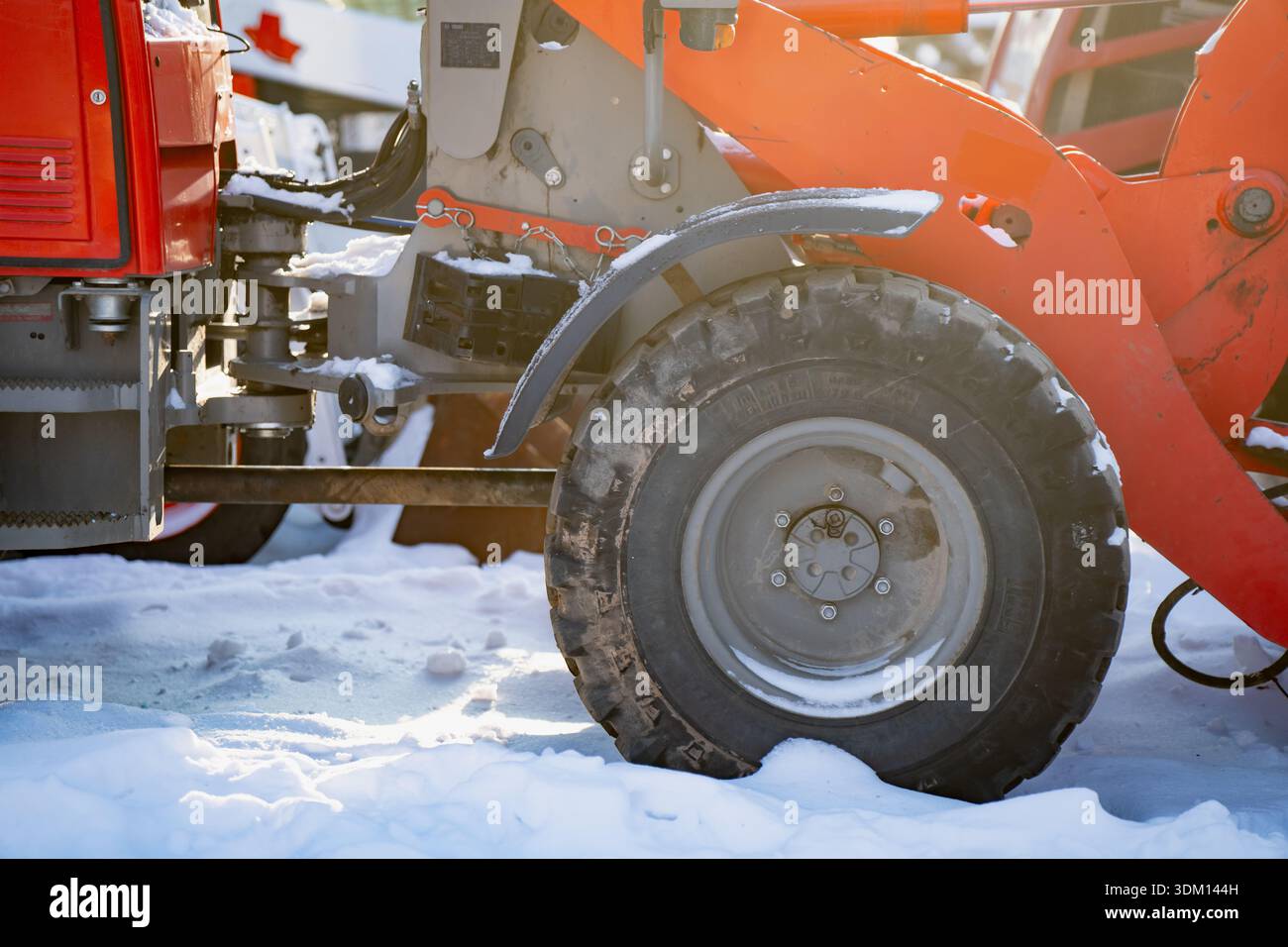 Industriefahrzeug mit großem Reifen, teilweise im Schnee vergraben, orangefarbener Laderrahmen und sichtbare Hydraulikkomponenten, Wintermaschinen auf der Baustelle Stockfoto