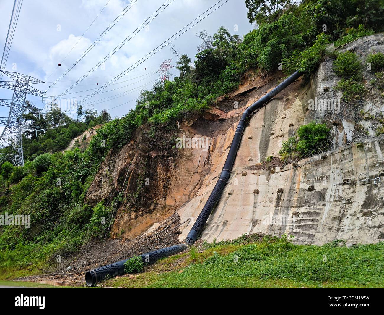 Ein langes industrielles HDPE-Abflussrohr, das an einem Stahlbetonhang entlang verläuft. Die Szene zeigt Erosionskontrolle und Infrastruktur in der Nähe eines Waldes und Hi Stockfoto