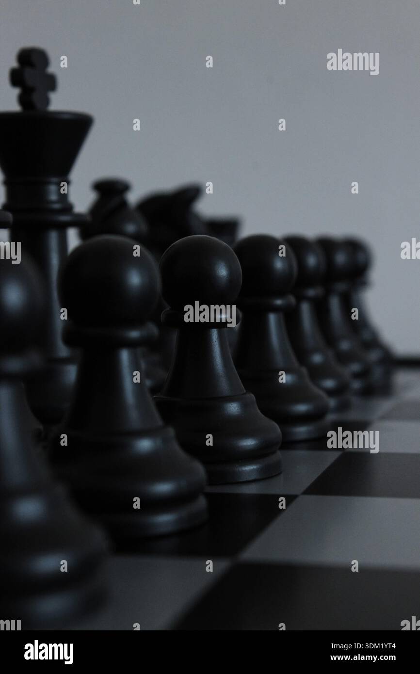 Schwarze Schachfiguren auf einem Schachbrett mit dunklem, minimalistischem Hintergrund. Symbol für Macht, Wettbewerb, Führung, Risiko, Strategie und Geschäft Stockfoto