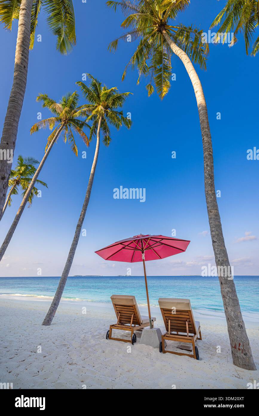 Zwei Holzsonnenliegen unter rotem Sonnenschirm im Schatten einer Palme an einem weißen Sandstrand. Ruhiges türkisfarbenes Meer. Familiensommerurlaub, Reiseurlaub, Paradiesurlaub Stockfoto