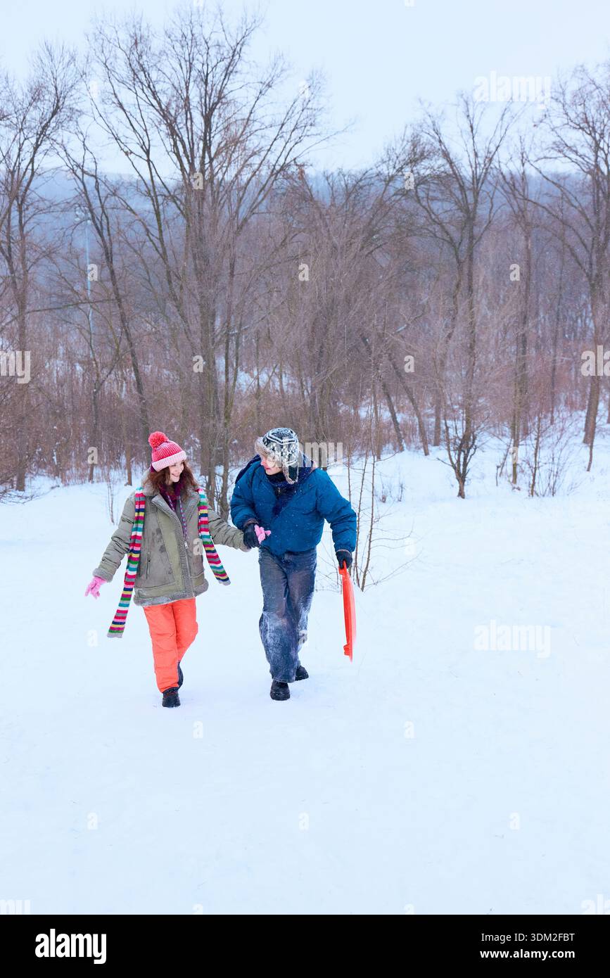 Freunde, die durch den verschneiten Park laufen, mit einem Schlitten und lächeln Stockfoto