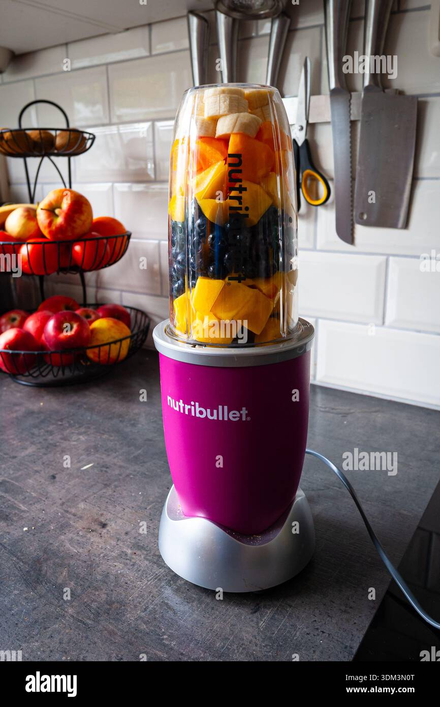 Lebendiger Fruchtmixer Nutriblender auf der Küchenzeile mit frischen Mangos, Pfirsichen und Bananen Stockfoto