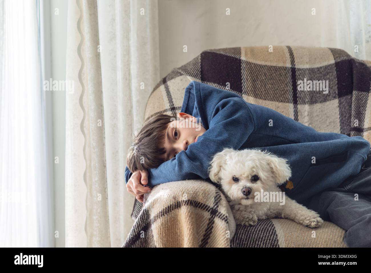 Kind mit Autismus entspannt mit Therapiehund zu Hause. Emotionale Verbindung zwischen Kind und Haustier, ruhige familiäre Atmosphäre, Wärme, Komfort und Alltag Stockfoto