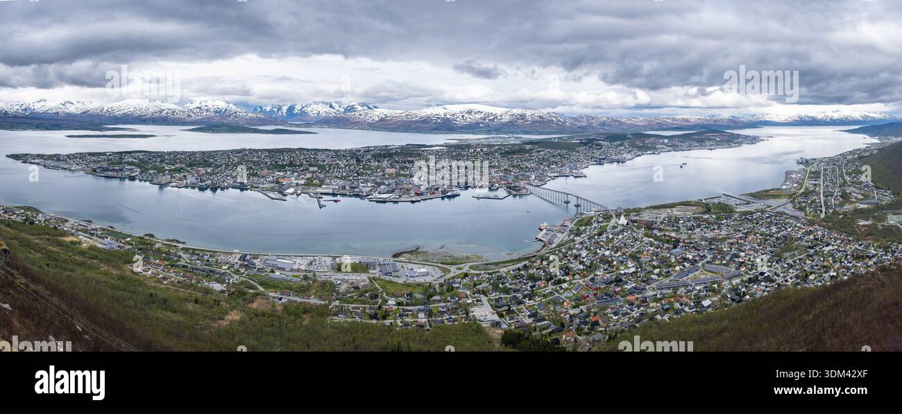 Ultrabreiter Panoramablick vom Storsteinen aus zeigt die gesamte Stadt Tromsø, die sich entlang des Fjords ausbreitet, eingerahmt von fernen schneebedeckten Bergen Stockfoto