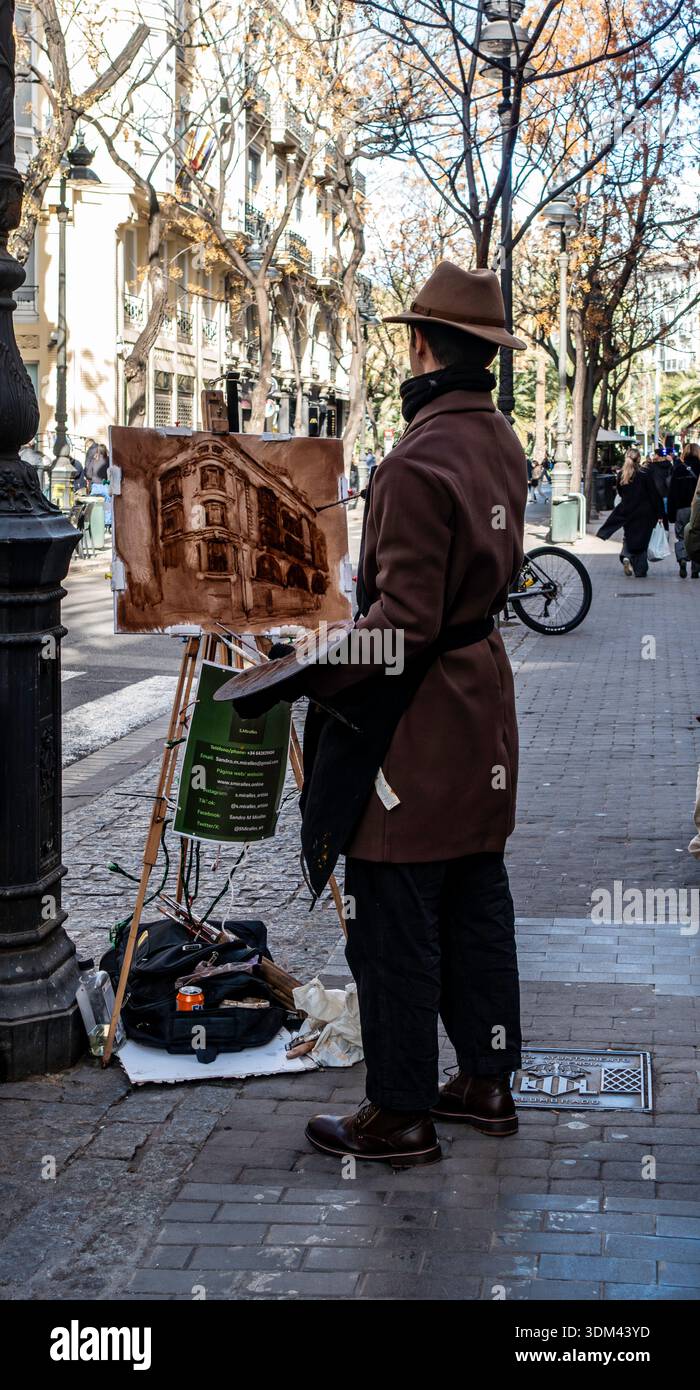 Der Straßenkünstler Sandro M. Miralles trägt einen Fedora und einen braunen Mantel, während er an seiner Staffelei auf einem Bürgersteig in Valencia, Spanien, ein monochromatisches Stadtbild malte. Stockfoto