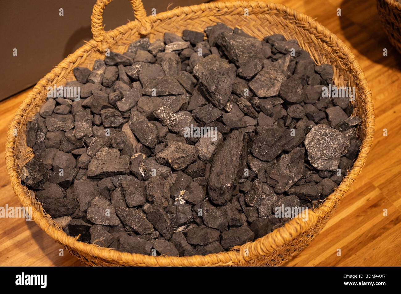 Nahaufnahme von Rohkohlebrocken, die einen traditionellen Esparto-Korb füllen und die Textur des Minerals und der Korbfasern auf einem Holz hervorheben Stockfoto