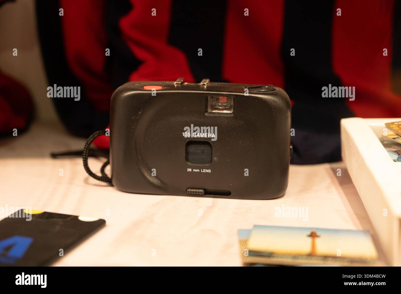 Nahaufnahme einer schwarzen, einfachen 135-Filmkamera (28-mm-Objektiv) auf einem Schreibtisch, umgeben von alten Fotos und Fotozubehör, die an Nostalgie der 90er Jahre erinnern. Stockfoto