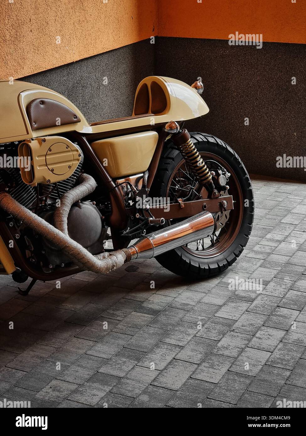 Nahaufnahme eines cremefarbenen alten Motorrads. Seite eines Oldtimer-Motorrads, nach rechts geparkt auf grauen Steinpflastern vor einer minimalistischen zweifarbigen Wand. Stockfoto