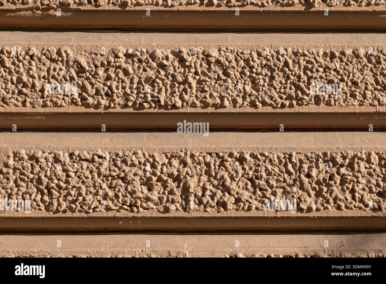 Rauer Stippelstuck mit horizontalen Bändern an einer sandbraunen Gebäudefassade Stockfoto