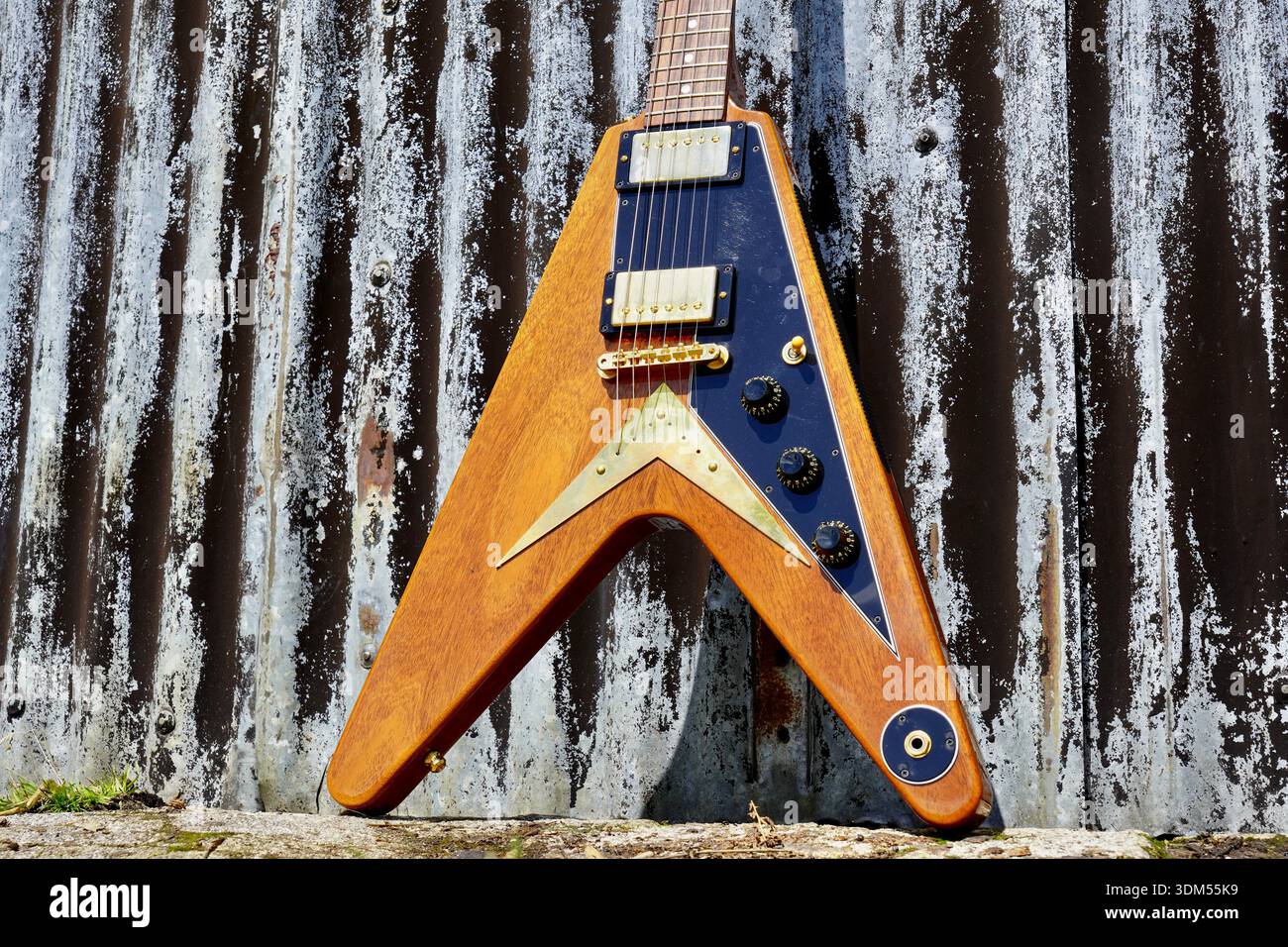 Fliegende V-E-Gitarre mit Goldbeschlägen vor rustikalem Metallhintergrund. Stockfoto