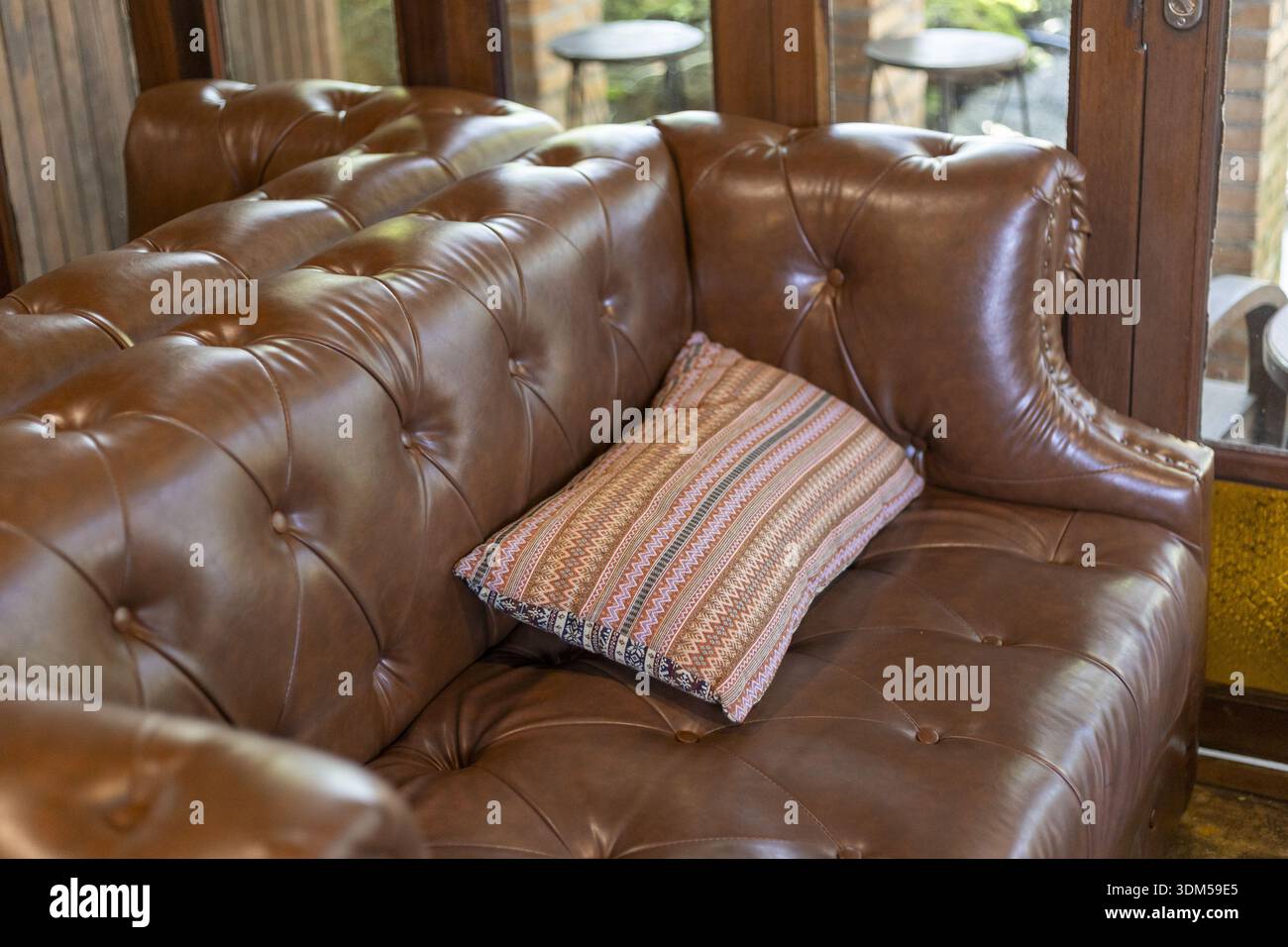 Komfortables braunes Ledersofa mit Kissen in klassischer Wohnzimmereinrichtung. Dieses Vintage-Möbelstück weckt ein Gefühl von gemütlicher Entspannung und Luxus Stockfoto