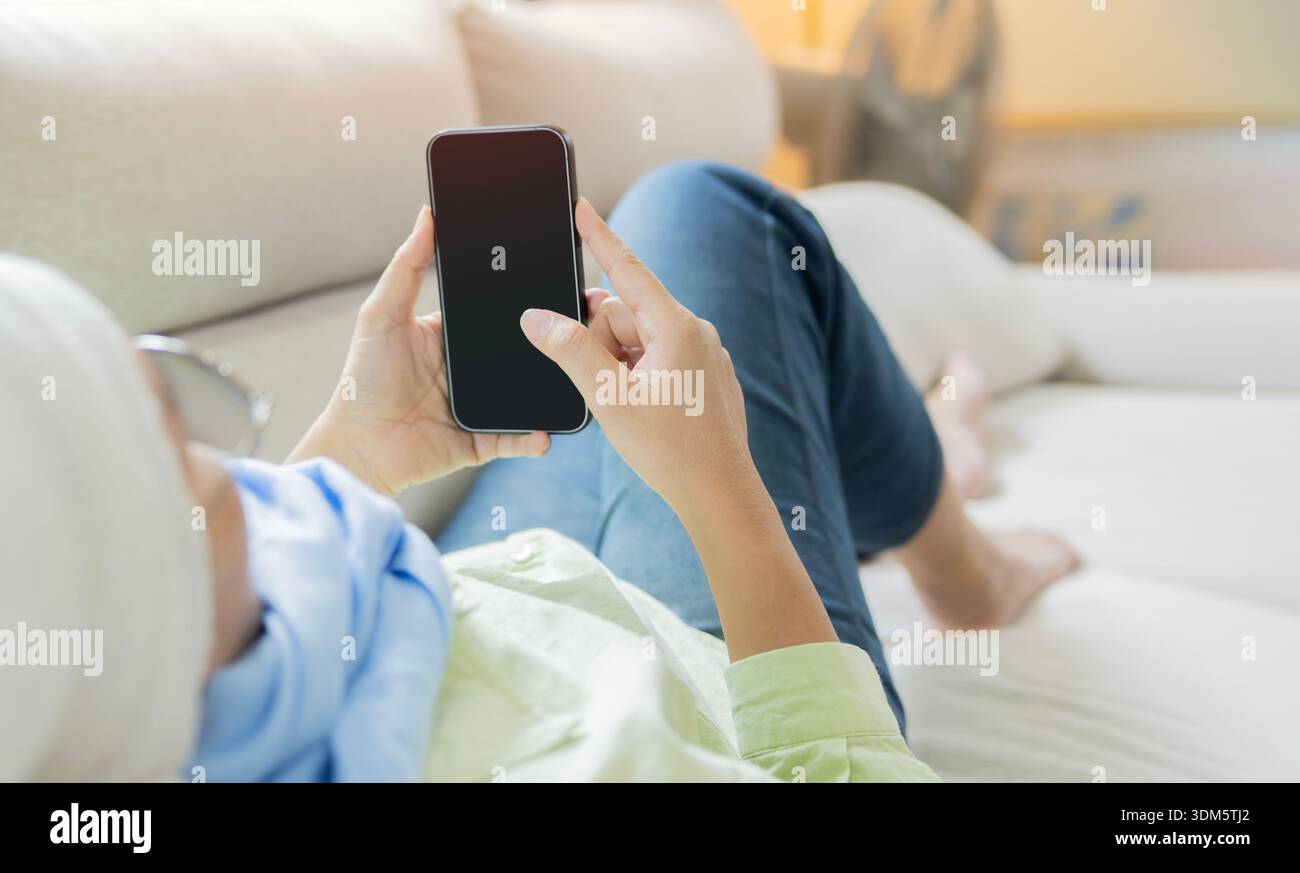 Rückansicht einer attraktiven Frau mit Krebs, legen Sie sich hin und genießen Sie die Entspannung per Telefon zu Hause. Krebsüberlebender-Konzept. Stockfoto