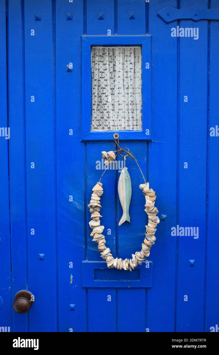 Muschelkranz und Holzfischdekoration hängen an einer blauen Haustür in einem Küstendorf in England, Großbritannien Stockfoto
