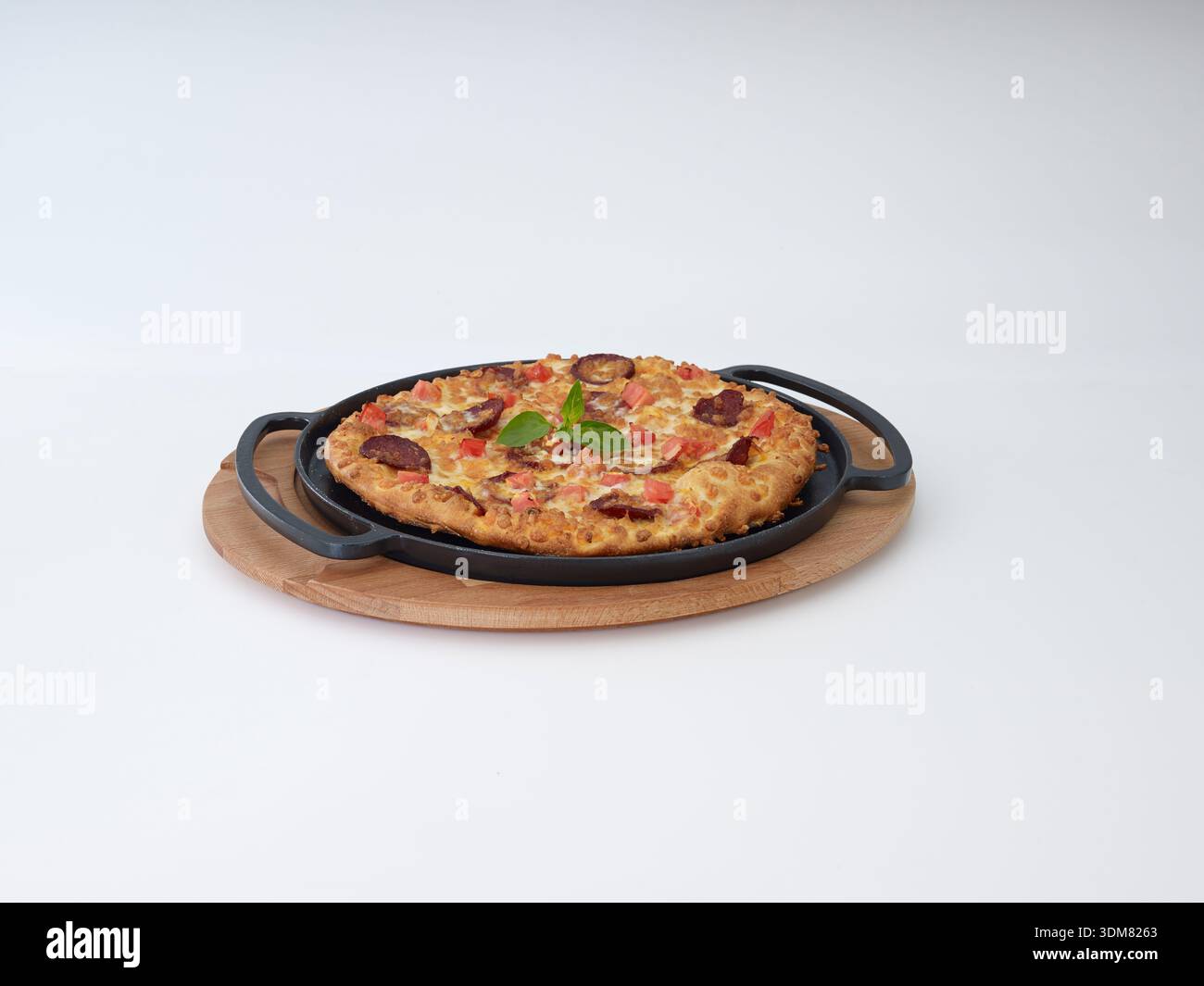 Wurst- und Tomatenpizza in gusseiserner Pfanne auf Holzbrett isoliert auf weiß Stockfoto