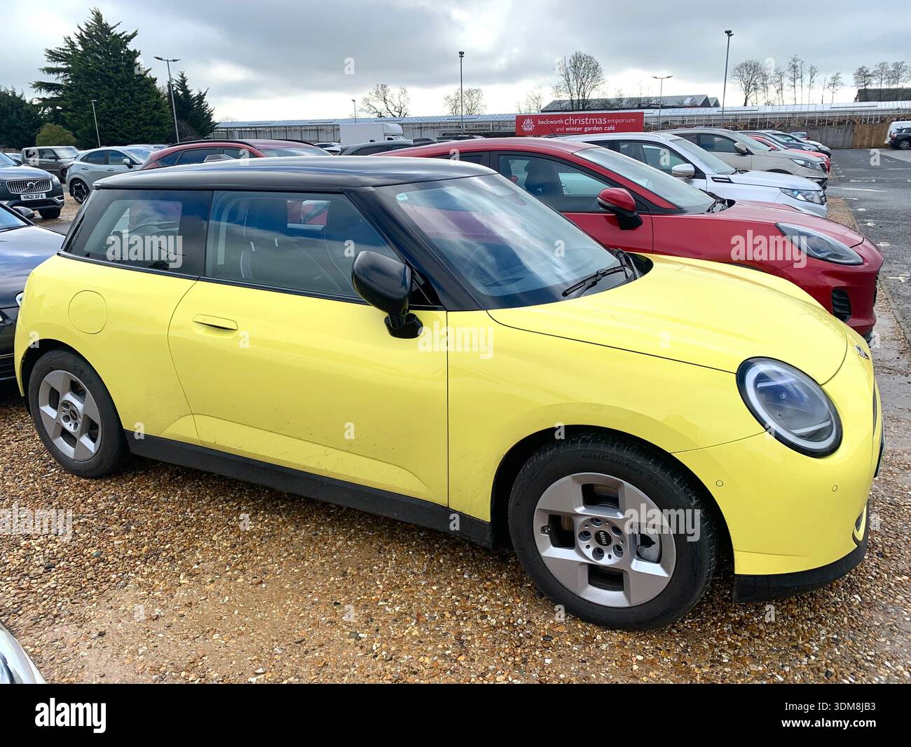 Gelbes und schwarzes ORA Elektroauto parkt in einem britischen Supermarkt Parkplatz Mini cooper S in der Nähe von Trolleys und anderen Fahrzeugen im Hintergrund - Smartphone-aufgenommenes Stockfoto