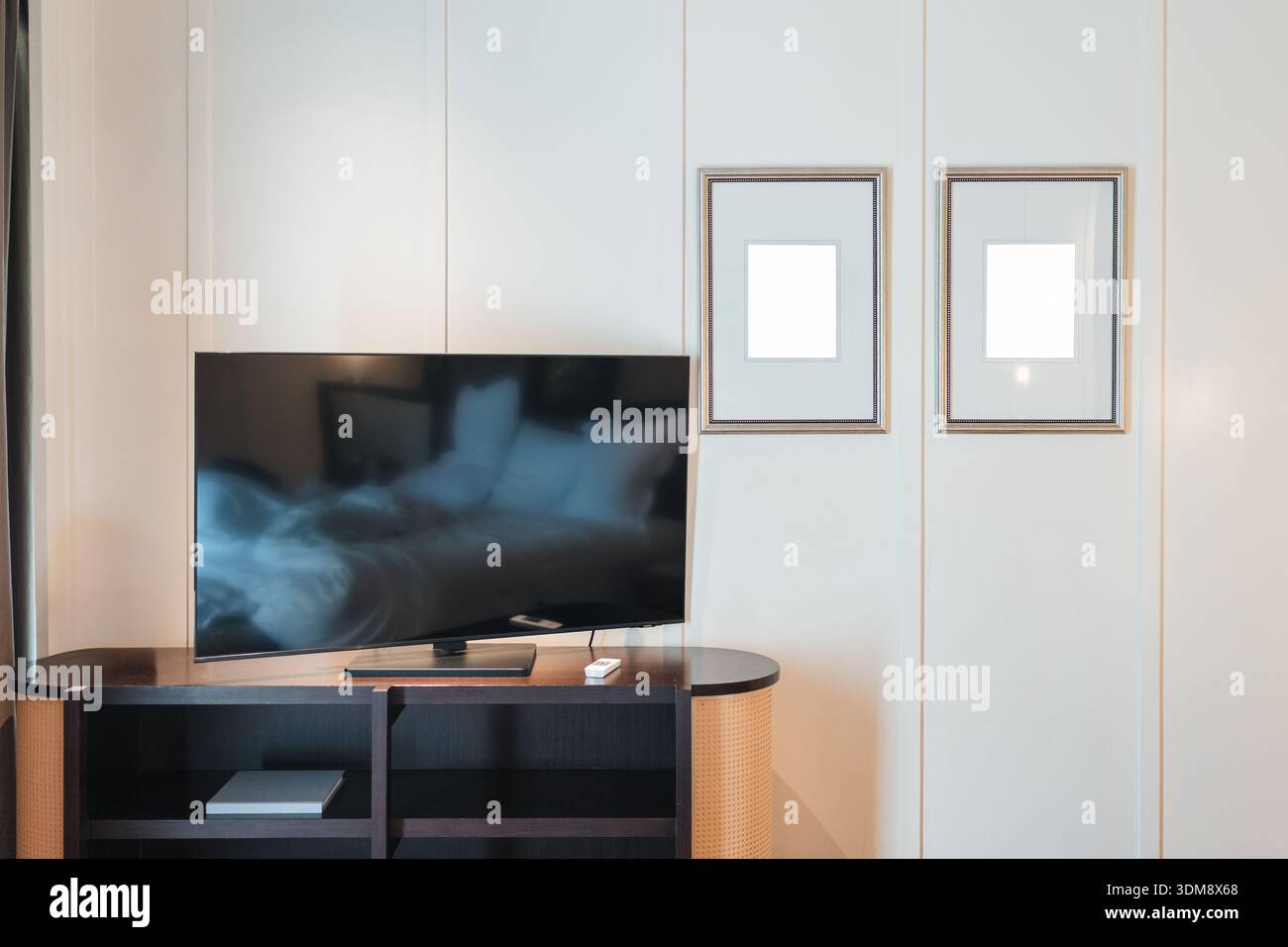 Modernes Hotelzimmer mit Flachbild-TV auf Holzständer, weißer Paneelwand und zwei minimalistischen Bilderrahmen Stockfoto