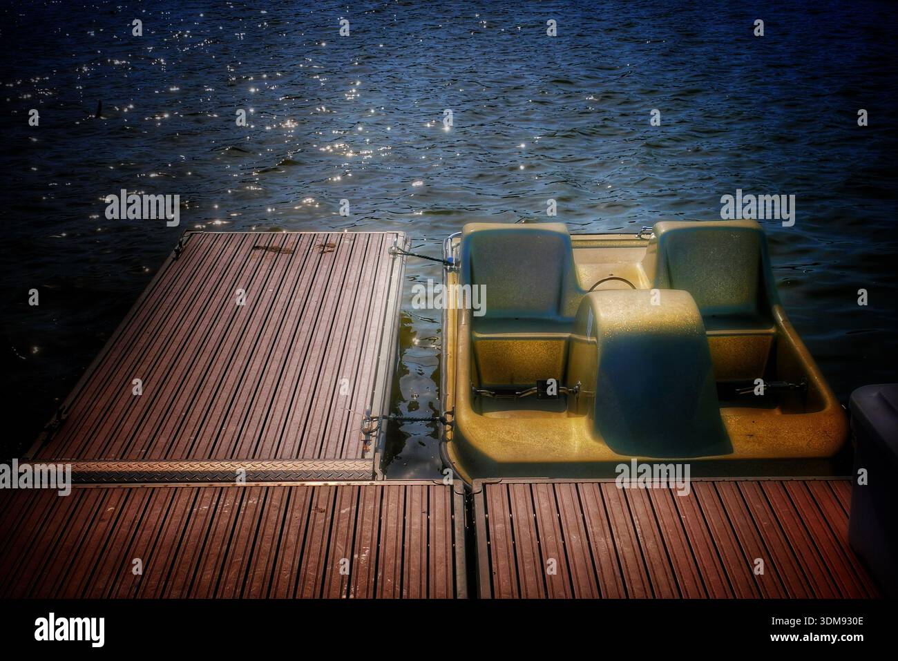 Ein ruhiges Tretboot ruht an einem sonnendurchfluteten Holzsteg Stockfoto