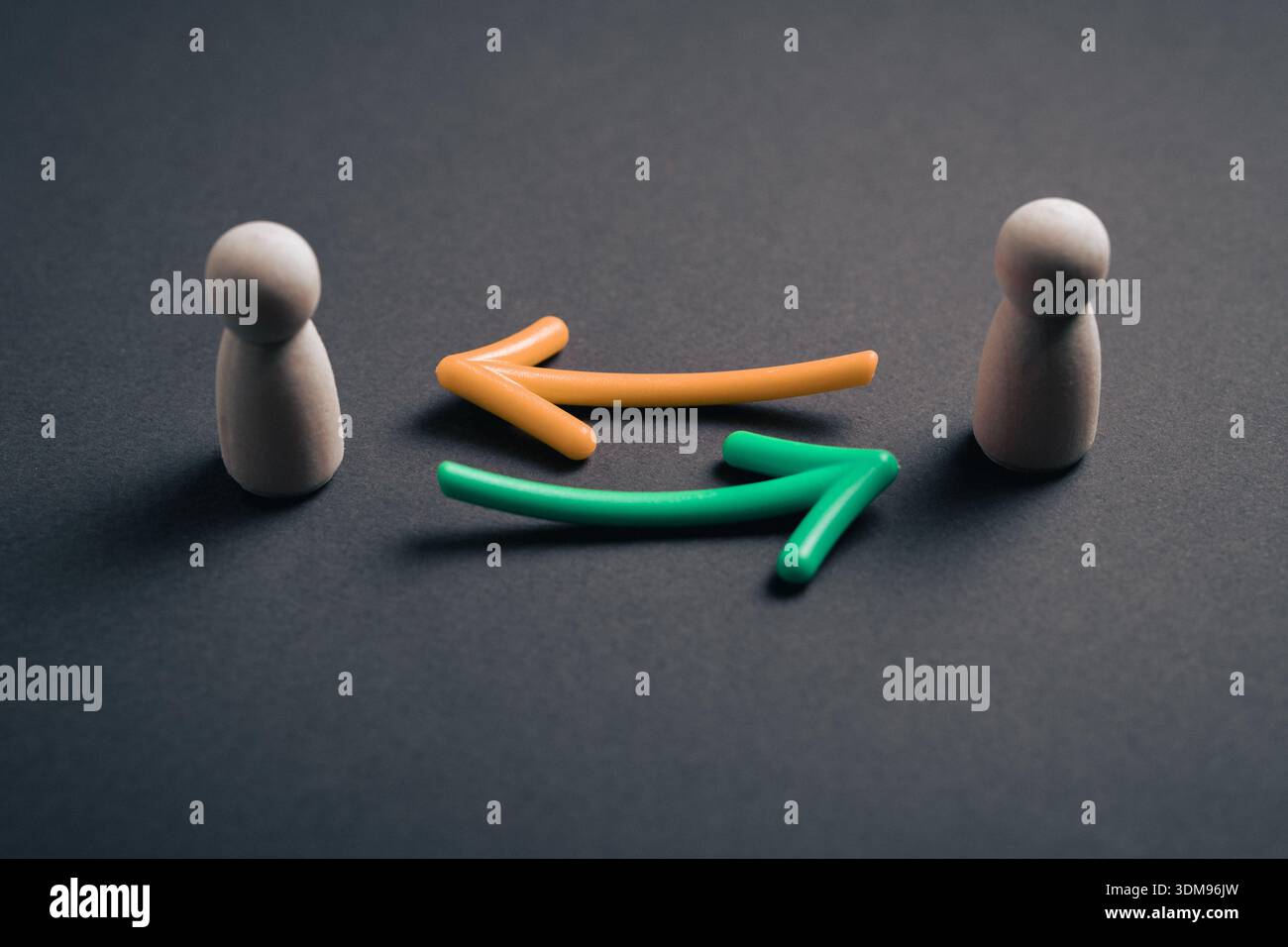 Zwei hölzerne Pfostenfiguren stehen einander gegenüber, mit orangefarbenen und grünen Pfeilen, die eine kontinuierliche Rückkopplungsschleife und eine effektive Kommunikation zwischen ihnen anzeigen Stockfoto