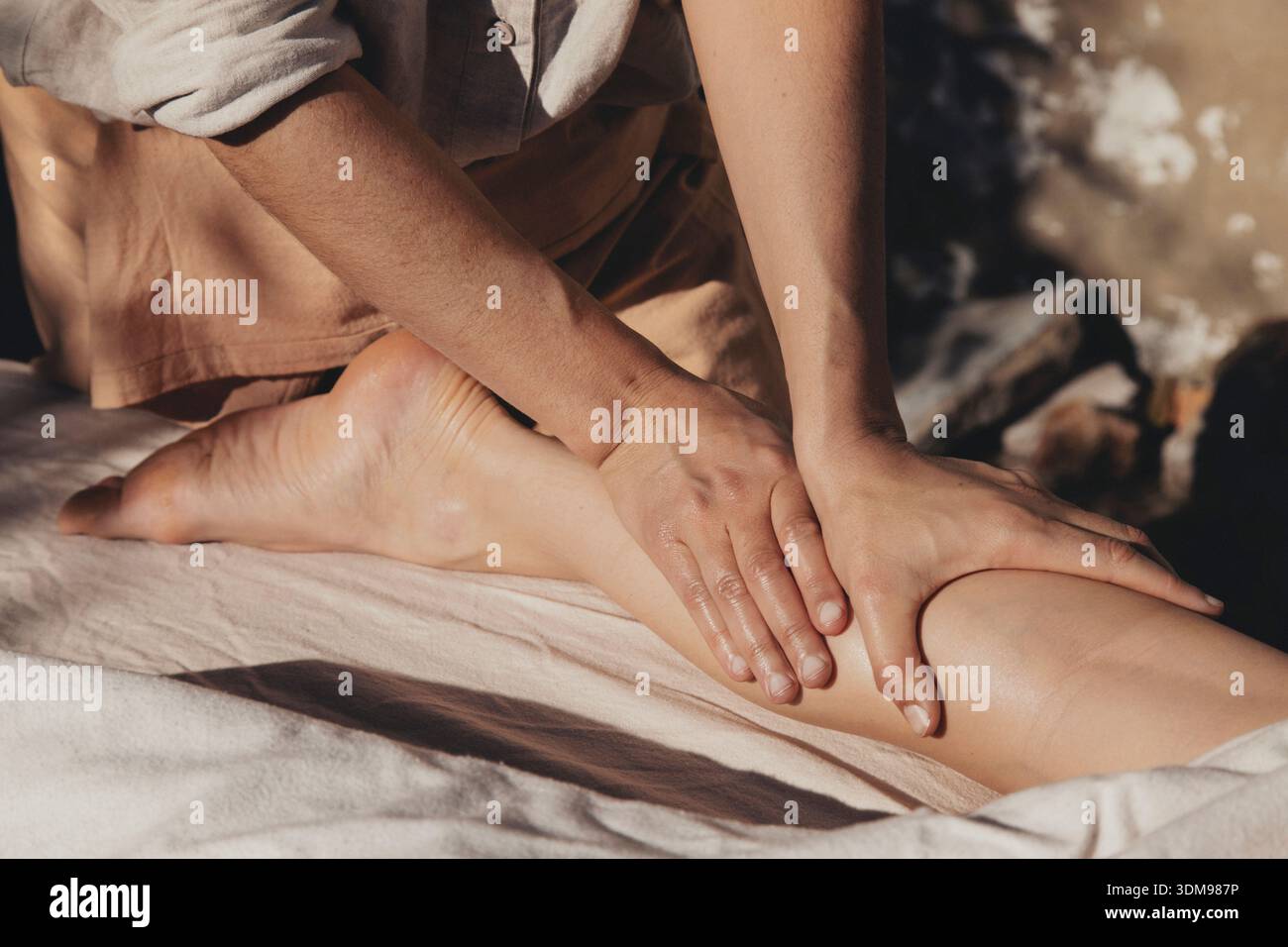 Ein Nahaufnahme-Foto, das eine entspannte Massagetherapie-Sitzung zeigt, bei der sanfte Hände dem Bein des Kunden Komfort und Entspannung bieten Stockfoto
