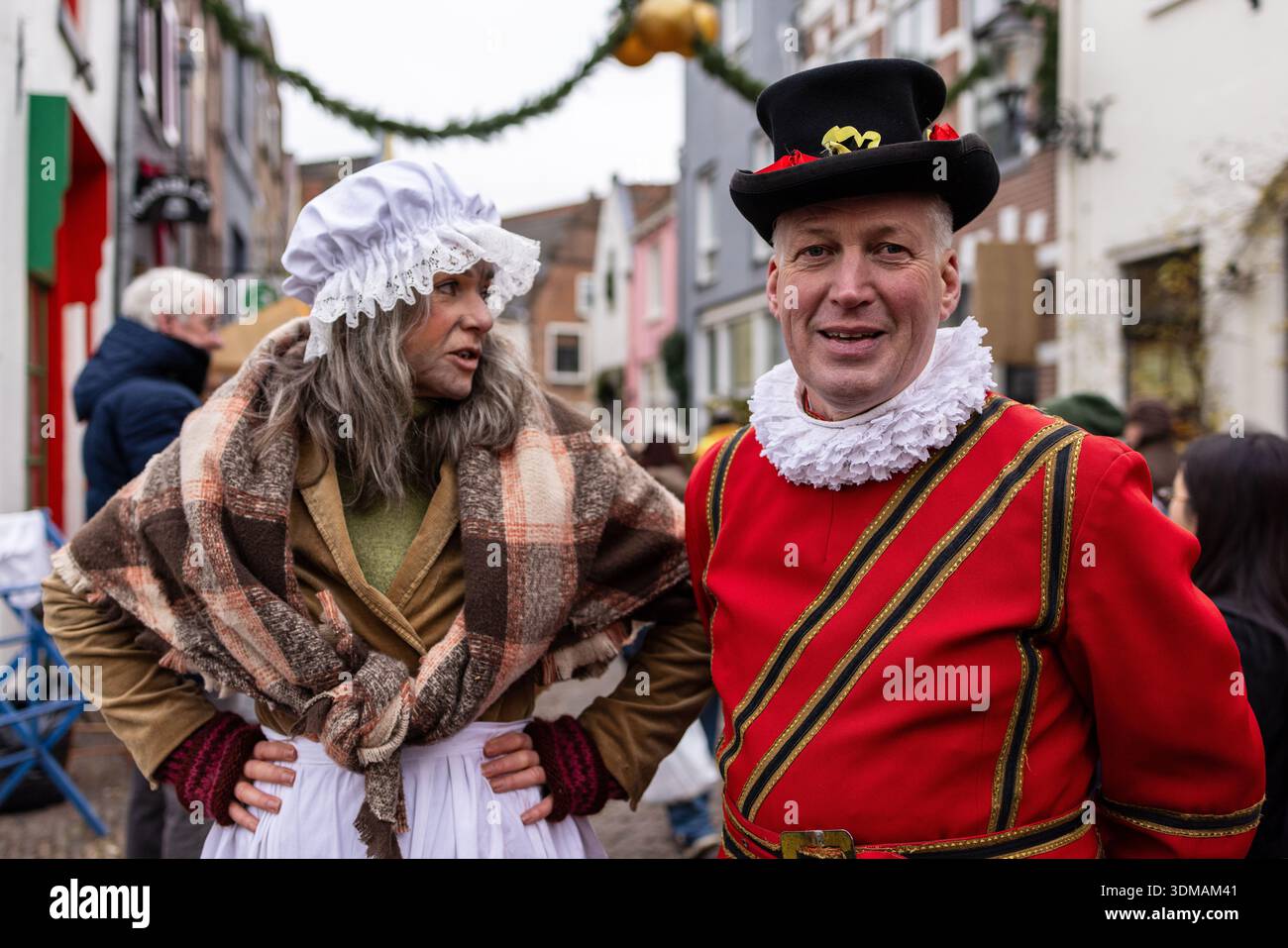 Deventer, Overijssel, Niederlande - 14.12.2025: Zwei Personen in festlichen historischen Kostümen stehen auf einer Kopfsteinpflasterstraße während einer Feiertagsveranstaltung. Stockfoto