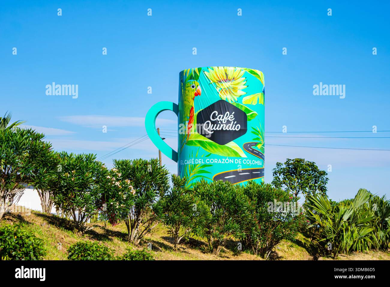 Filandia, Quindio, Kolumbien - 7. Dezember 2025 - bunte Kaffeetasse am hellblauen Himmel mit grünen Büschen im Vordergrund. Stockfoto