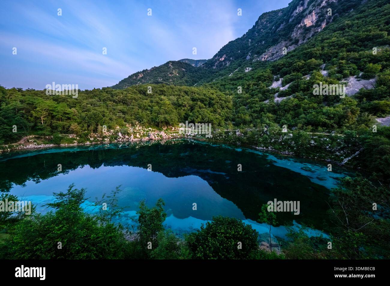 Tiefblauer Lago di Cornino, umgeben von üppig grünen, bewaldeten Bergen unter einem Dämmerungshimmel, der die Hänge im klaren Wasser reflektiert. Stockfoto