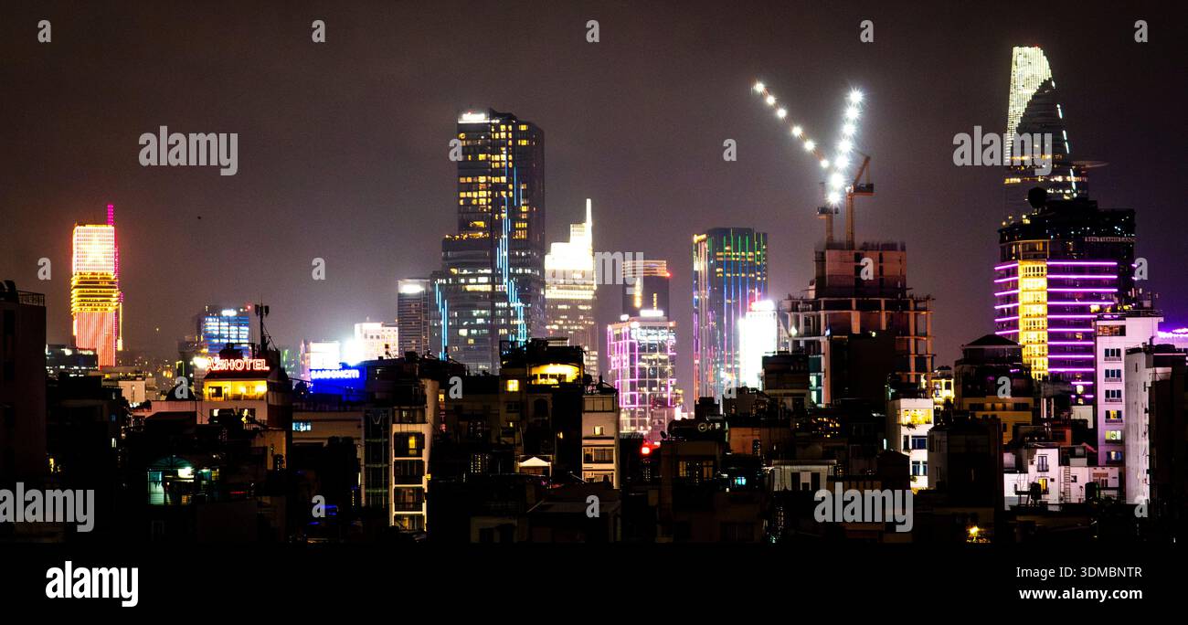 Skyline der Nachtstadt mit beleuchteten Hochhäusern, farbenfrohen Neonlichtern und einem Baukran, der eine V-Form im Vordergrund unter einem Hektar bildet Stockfoto