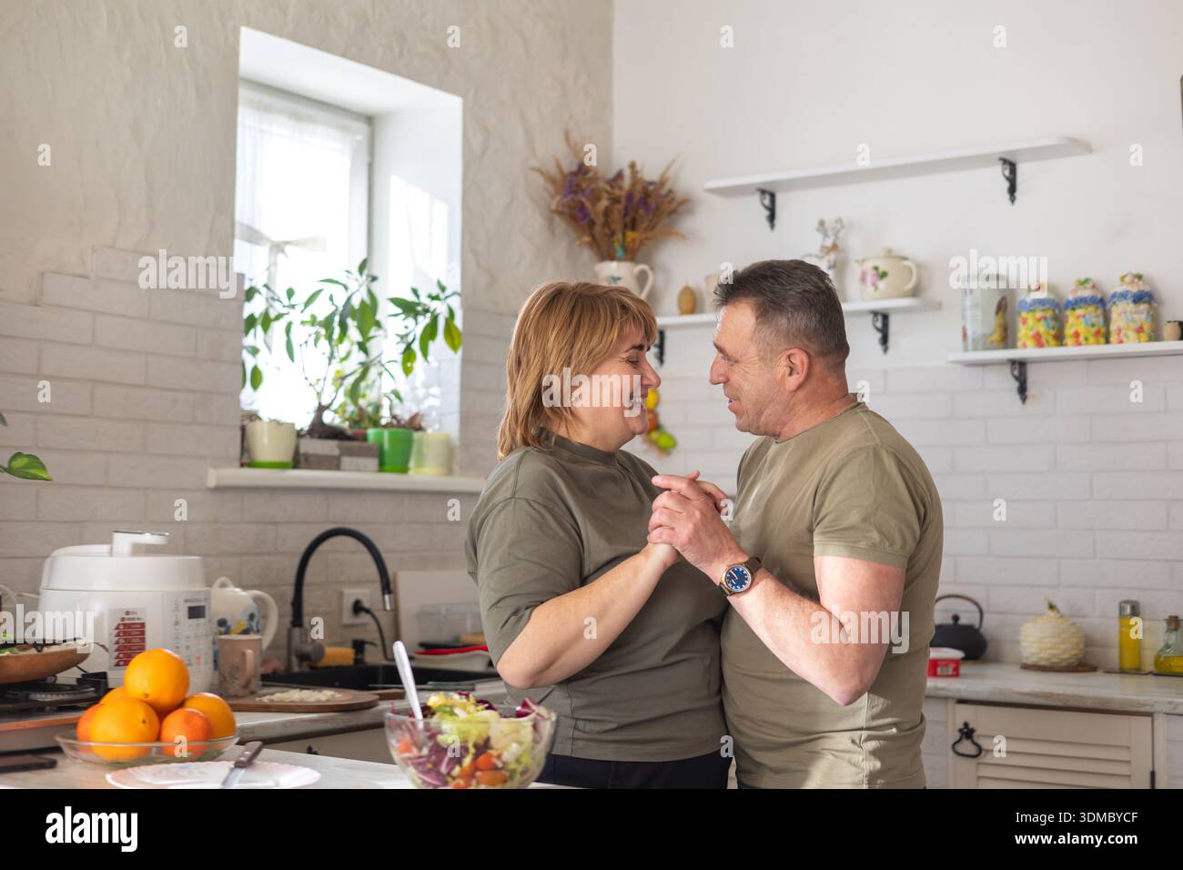 Ein reifes Paar teilt einen sanften, romantischen Tanz in ihrer Küche, während es zusammen Essen zubereitet. Ein warmer Tag der Liebe, der Verbindung, der Familie Stockfoto