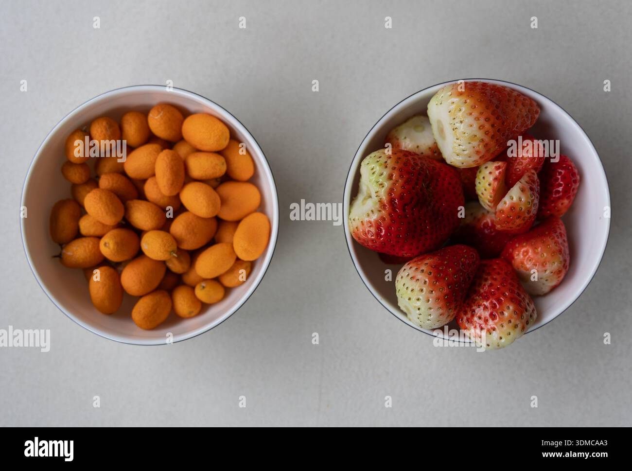 Frische Kumquats und Erdbeeren in weißen Schüsseln auf hellem Hintergrund, minimalistisches Essen flach gelegt. Stockfoto