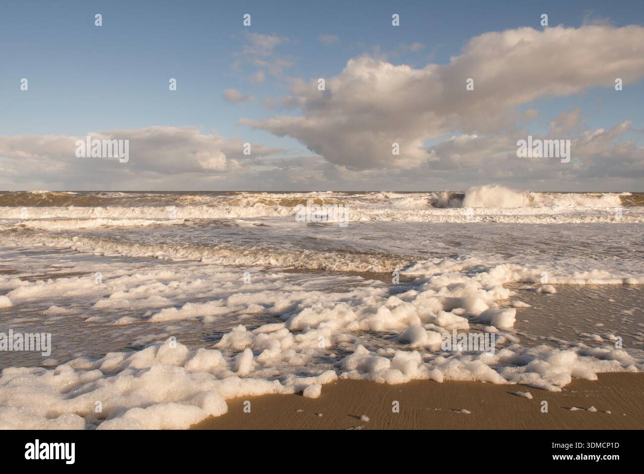Weißer Meeresschaum von einem stürmischen Meer, das am Strand in Walcott, Norfolk, Großbritannien, unter blauem Himmel auftaucht, jetzt ist der Sturm vorüber, Dezember Stockfoto