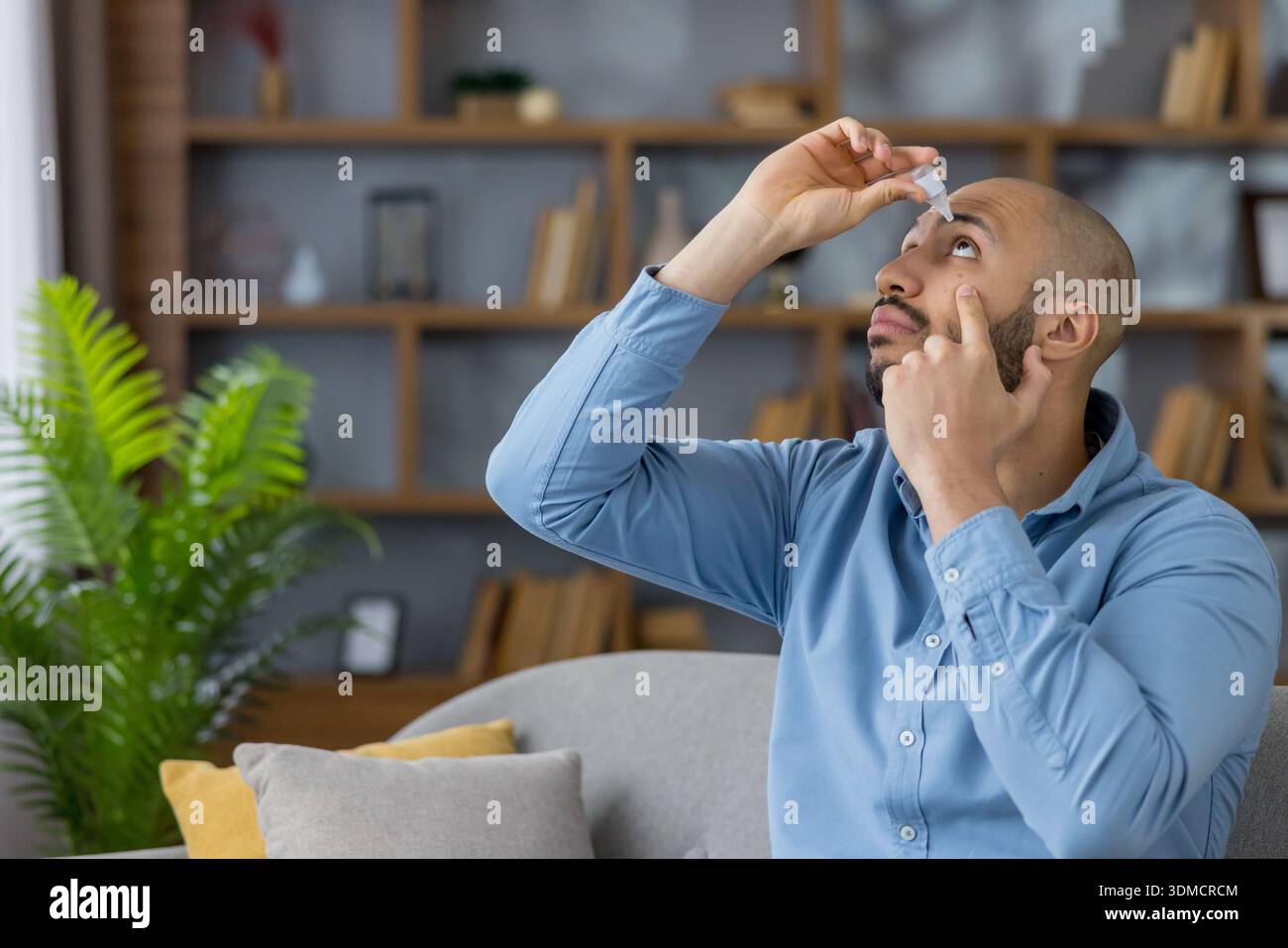 Mann wendet Augentropfen aus einer kleinen medizinischen Flasche an, behandelt trockene Augen und übt Selbstpflege zu Hause mit sanfter Präzision für Linderung, Feuchtigkeit und tägliche Augengesundheit Stockfoto