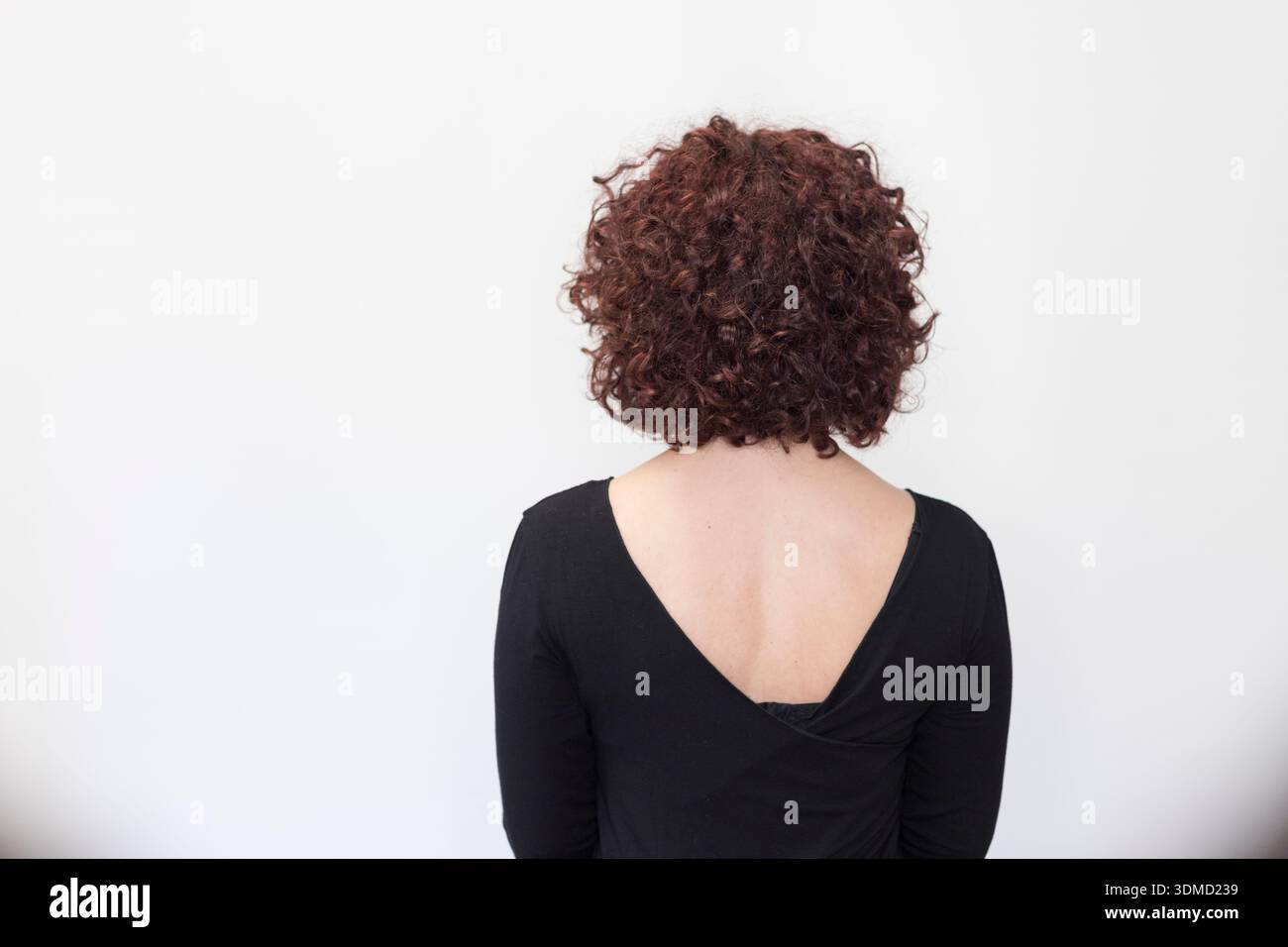 Eine Aufnahme im hinteren Studio nimmt eine Frau mit einer kurzen, voluminösen, lockigen bob-Frisur vor einem schlichten weißen Hintergrund auf. Der Fokus liegt auf der Rückseite des Hea Stockfoto